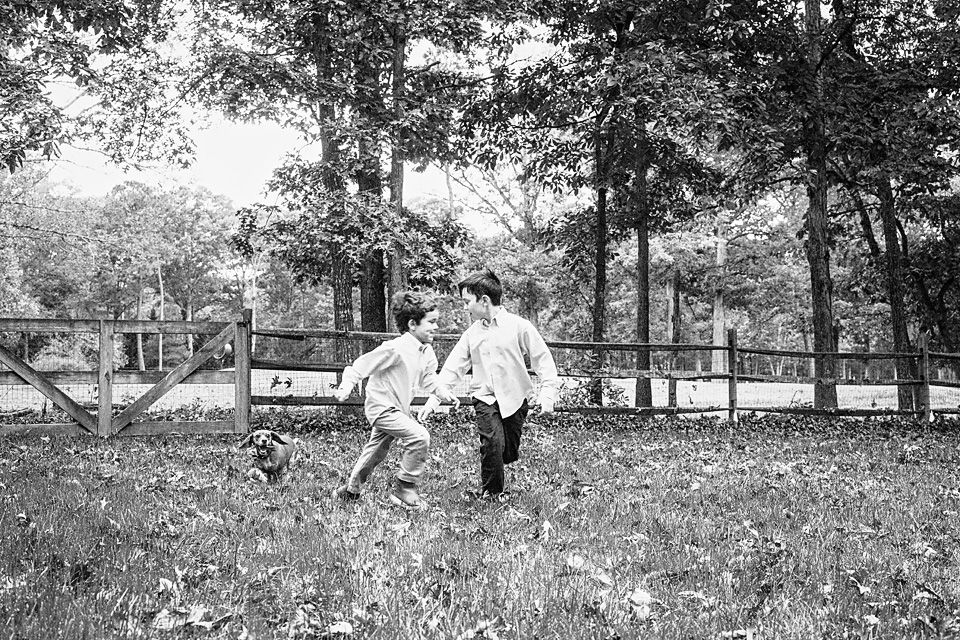 Two young boys run and play together in a lush green field in a classic black and white portrait Richmond VA family photography. Midlothian,
