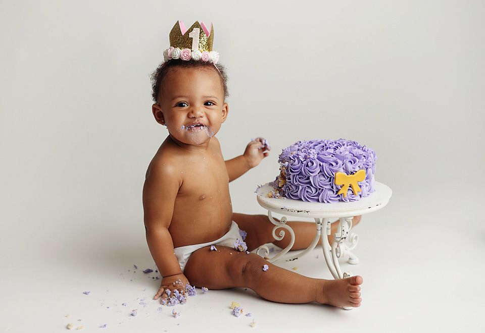 Baby's first birthday cake smash session with purple frosted cake and gold crown.