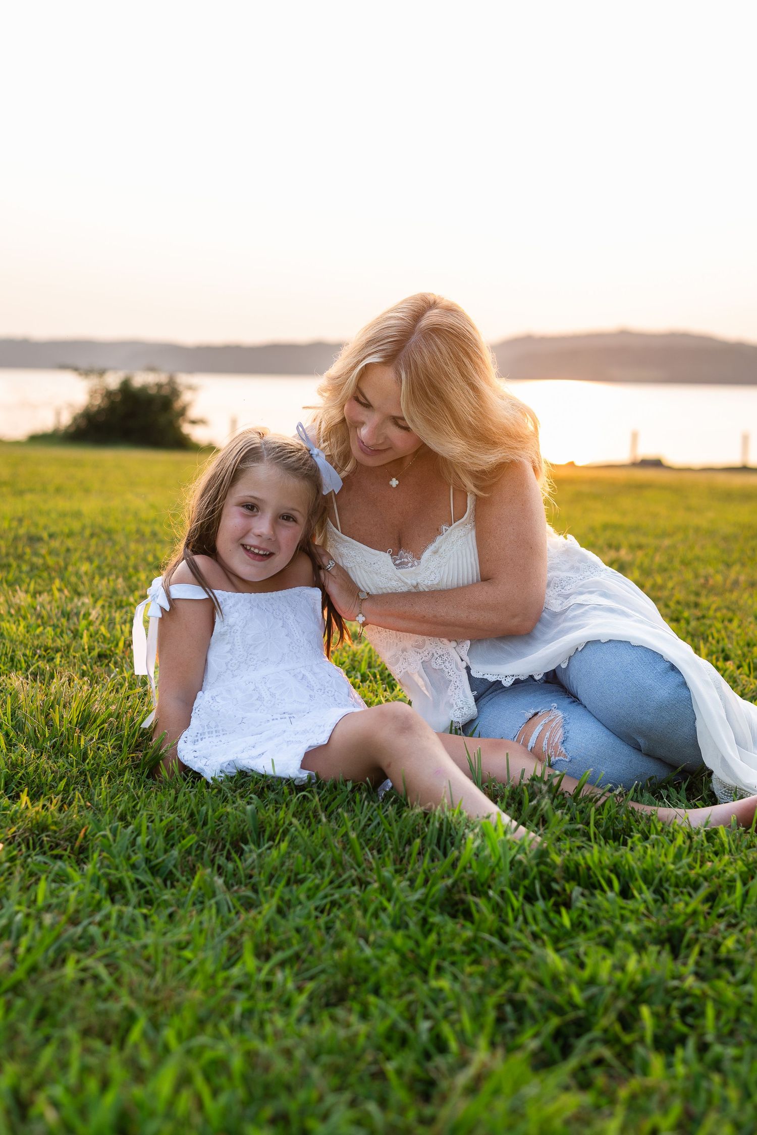 Family enjoying a tender moment together on grassy hill by the lake at sunset.