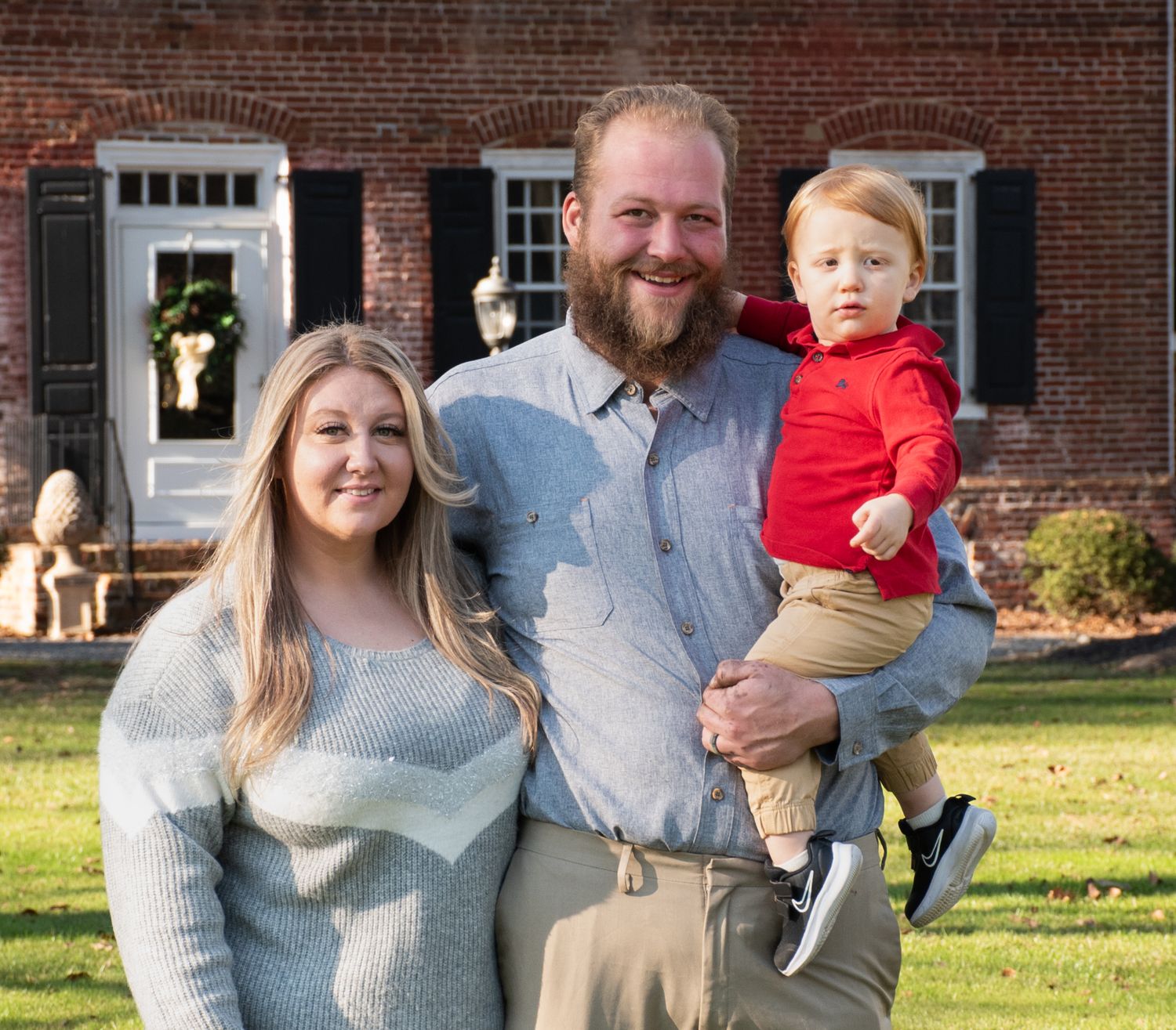 A family poses together on their front lawn in front of a classic brick house.