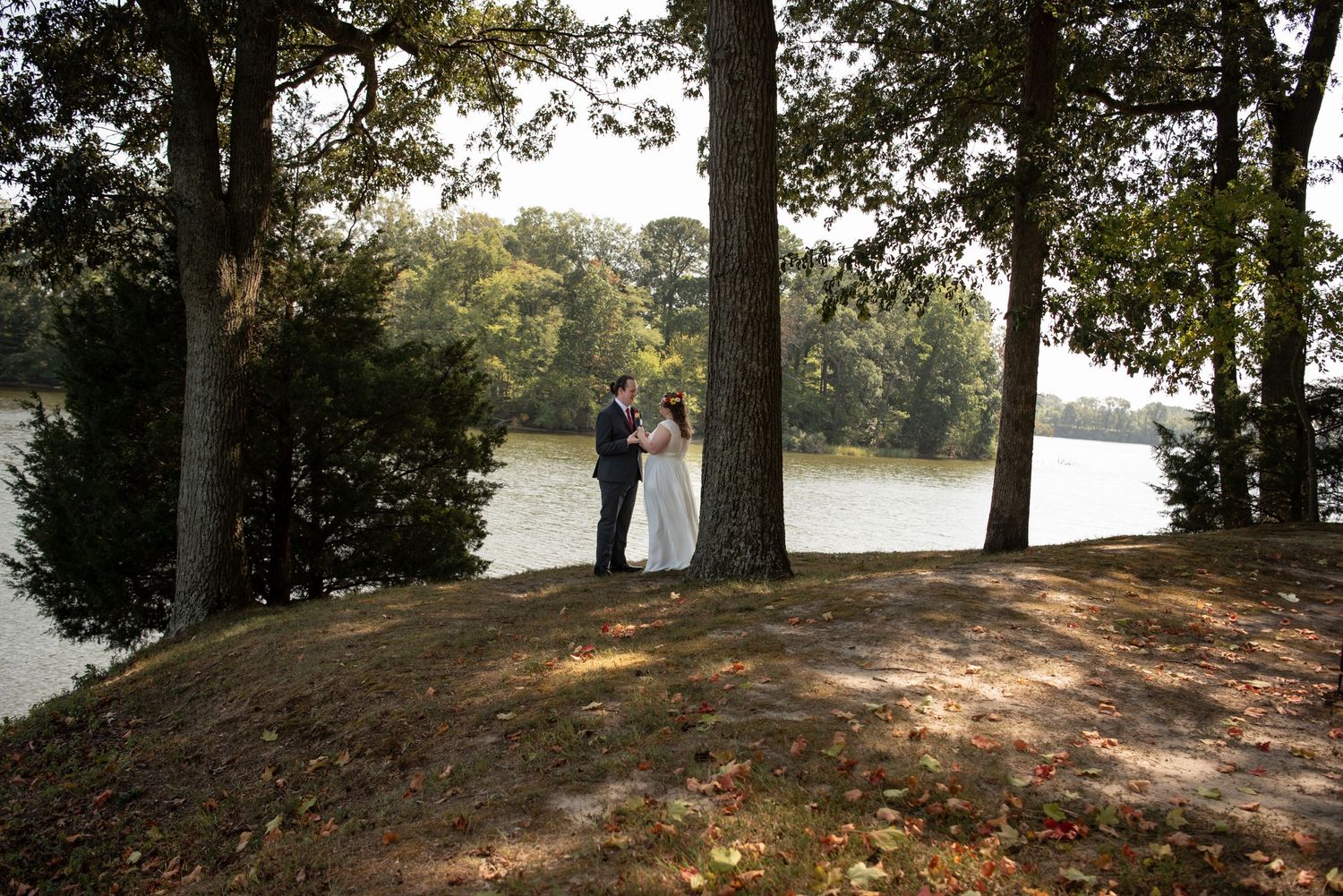 Wedding couple standing between trees overlooking serene lake.