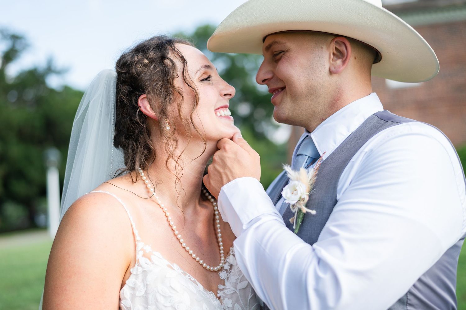 A joyful couple shares a tender moment on their wedding day, the bride in white and groom wearing a cowboy hat.
