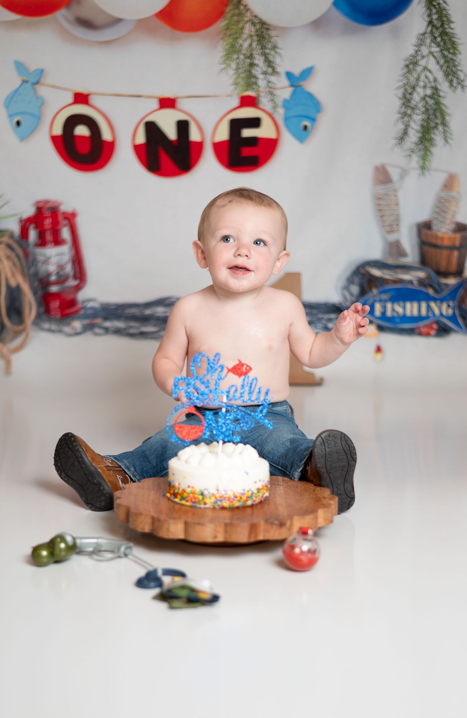 A first birthday celebration with a blue and white cake and colorful balloons in the background.