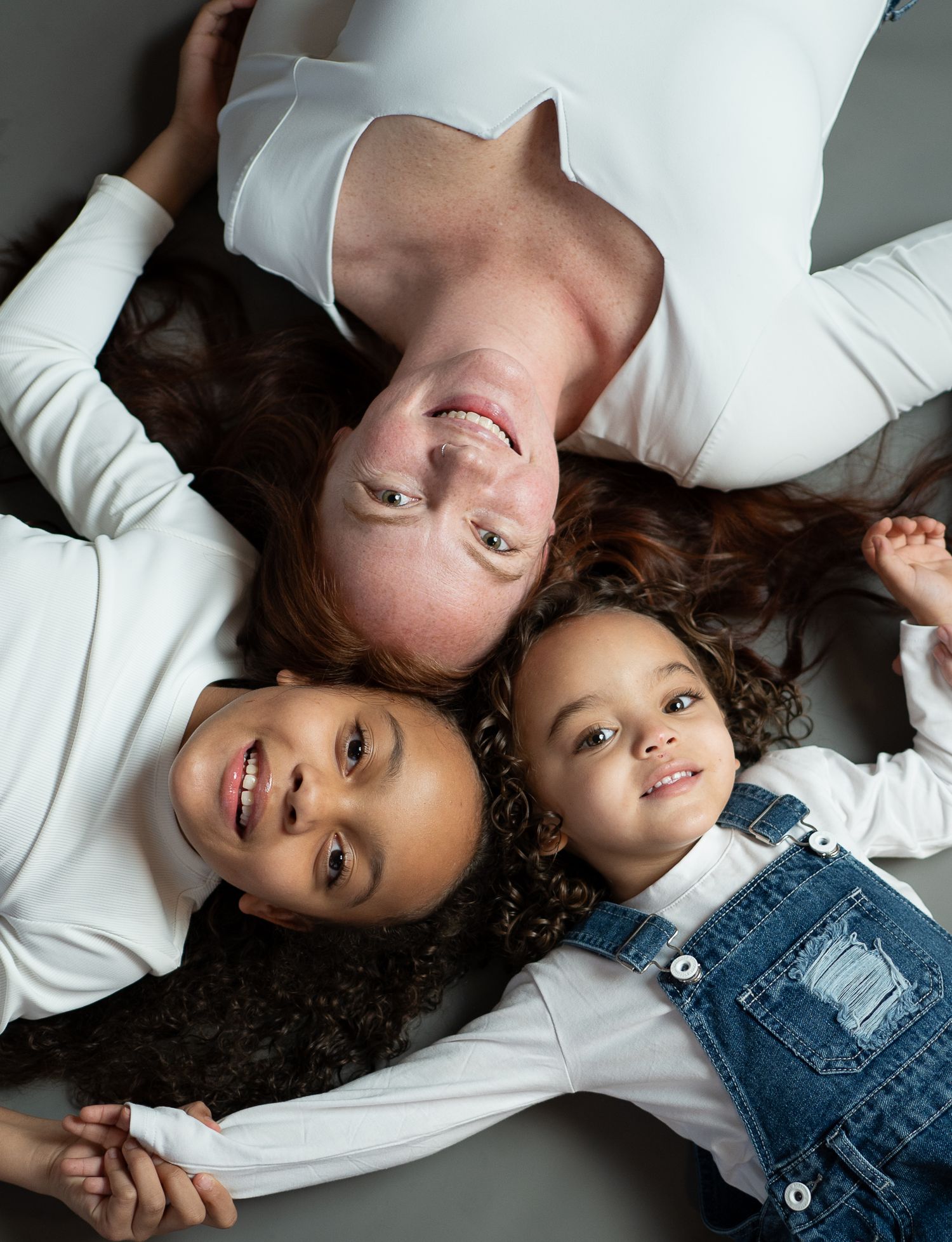 Two children lying on a white surface in denim overalls and white shirts smiling at the camera.