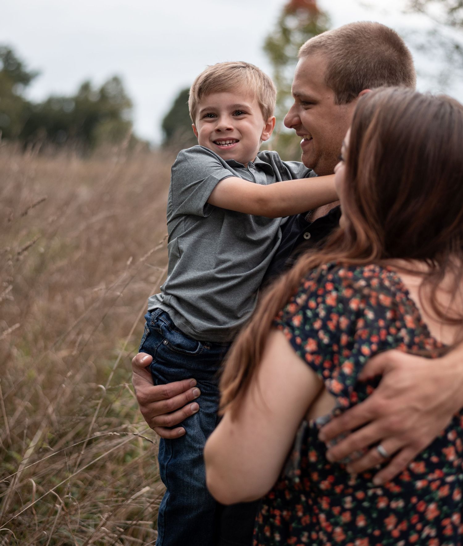 Joyful family moment captured in tall grass during outdoor photo session.