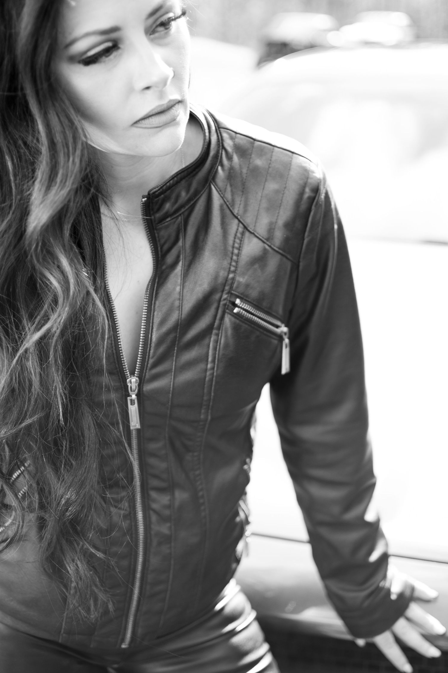 Black and white portrait of a woman in leather jacket with long wavy hair looking down.