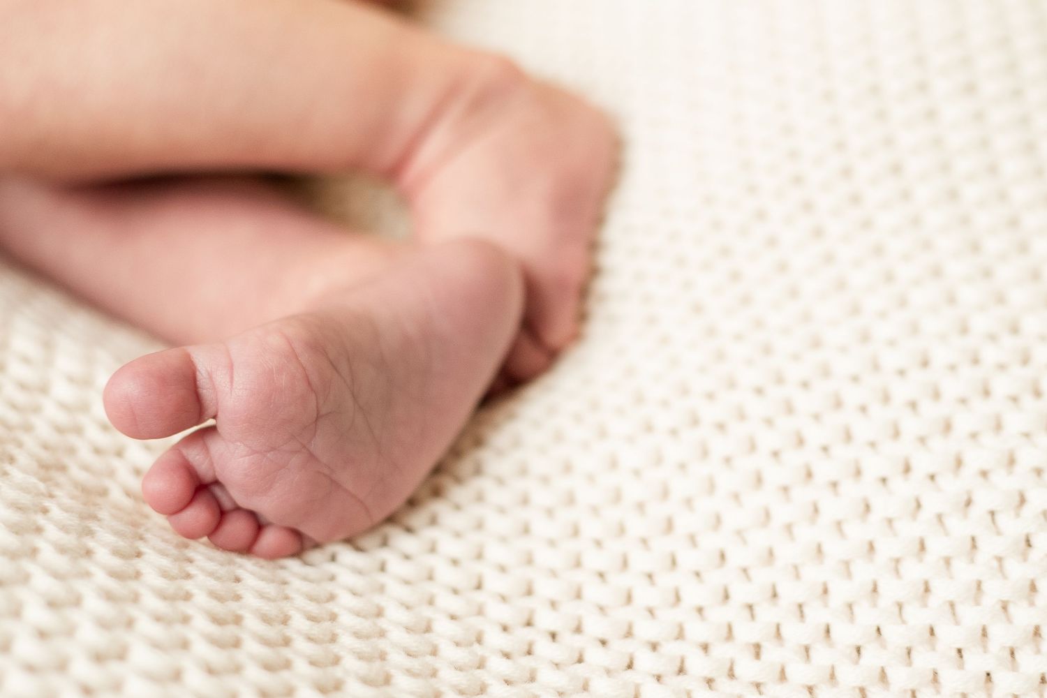 A tiny baby foot rests on a soft white knitted blanket in a gentle, peaceful close-up shot.