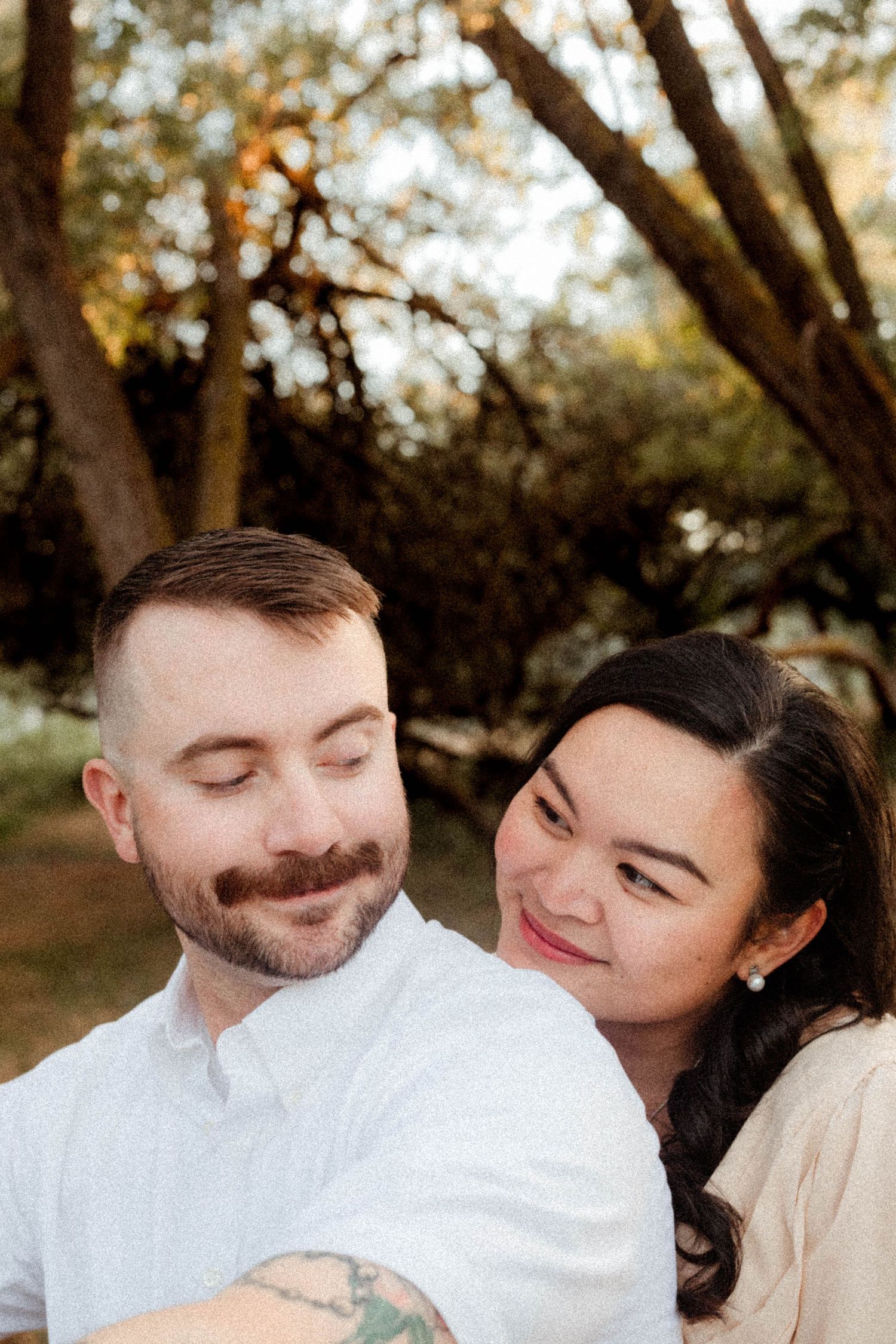 Smiling woman leans affectionately against her partner during a warm outdoor engagement photo session.