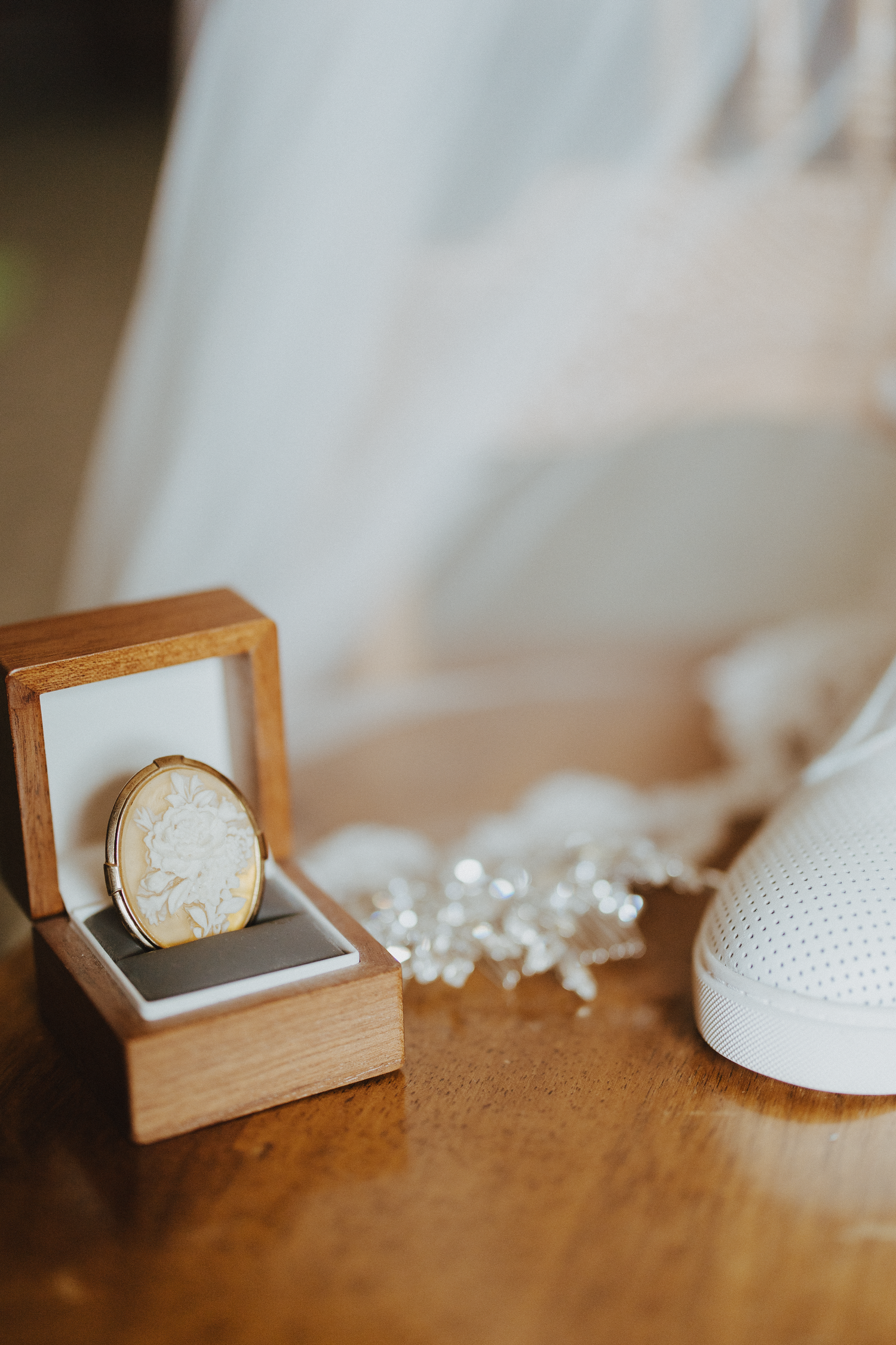 Gold locket in wooden box with white bridal shoe and veil on table.