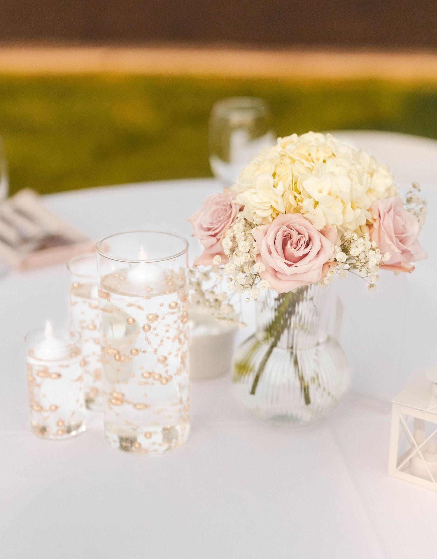 Elegant wedding centerpiece with pink roses, white hydrangeas, and floating candles on white table.