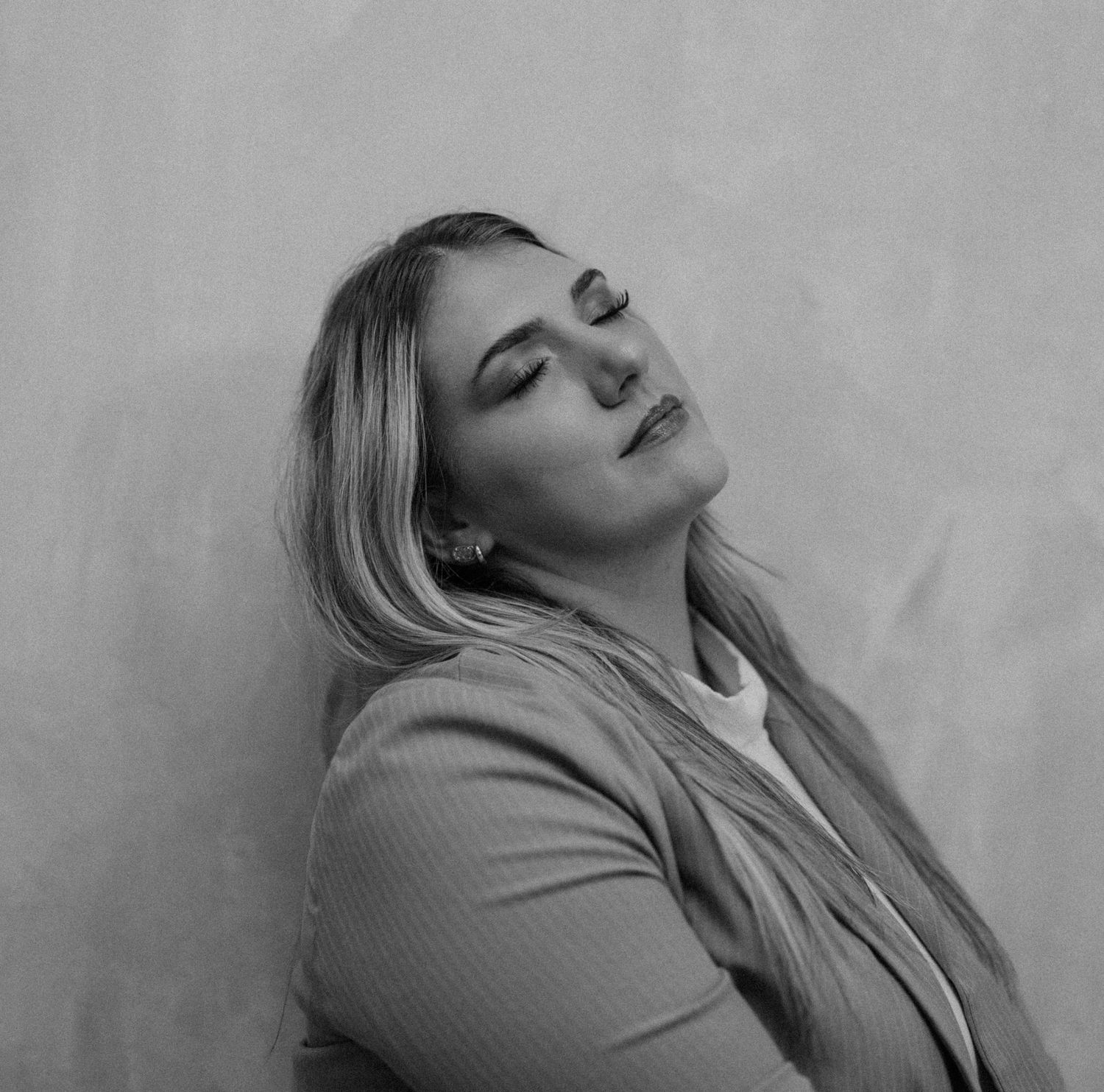 Black and white portrait of blonde woman leaning against wall with eyes closed.