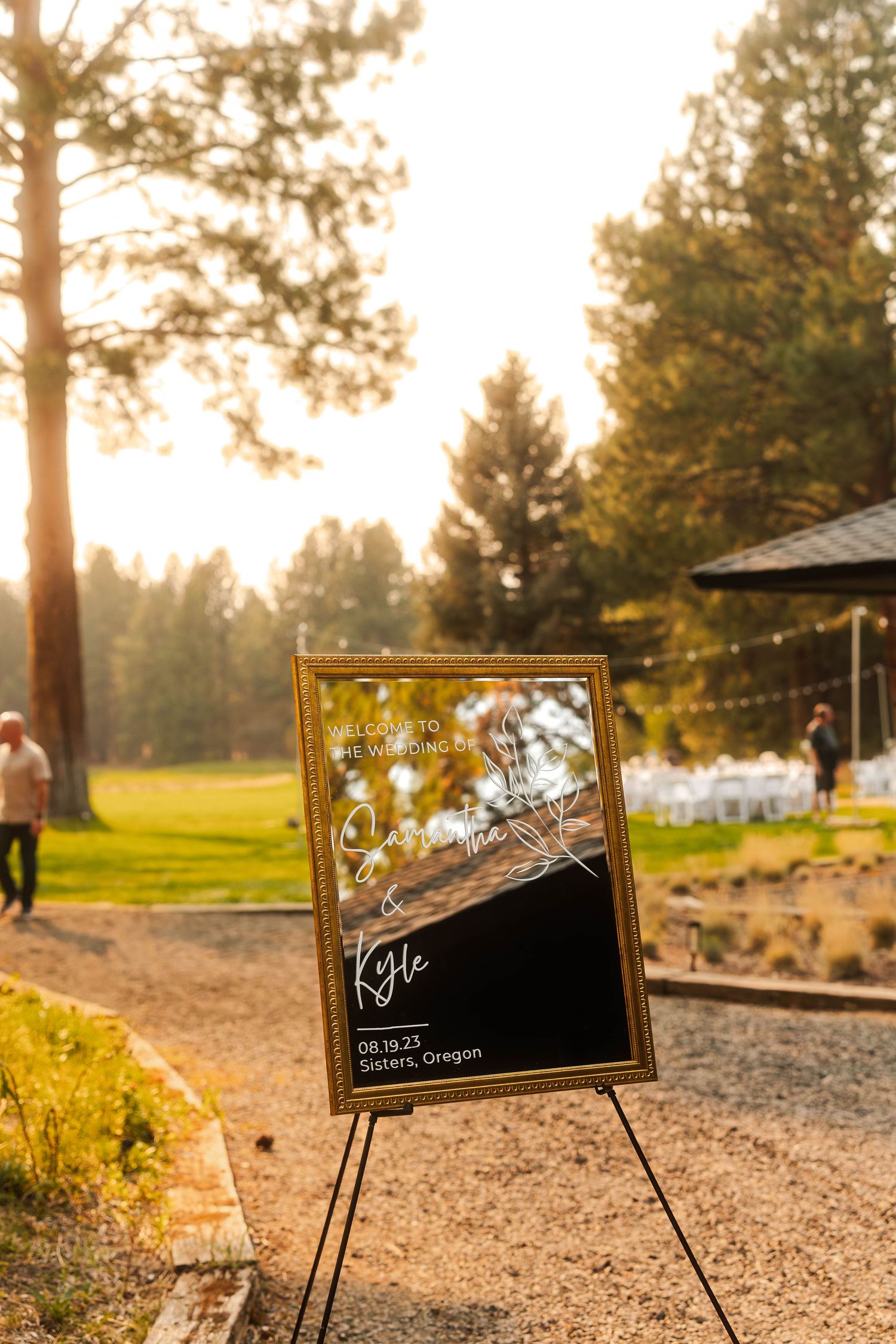 Gold-framed wedding welcome mirror sign on easel at outdoor venue in Sisters, Oregon at sunset.