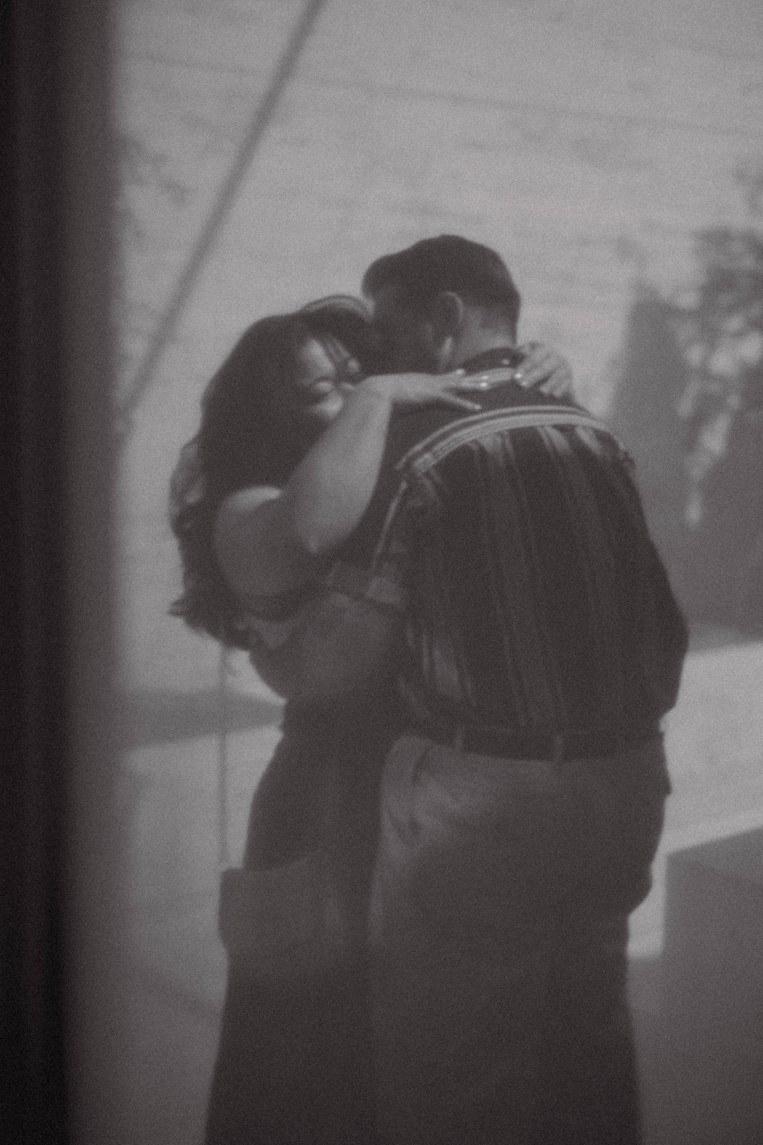 Black and white photo of a couple embracing and dancing together seen through a window.
