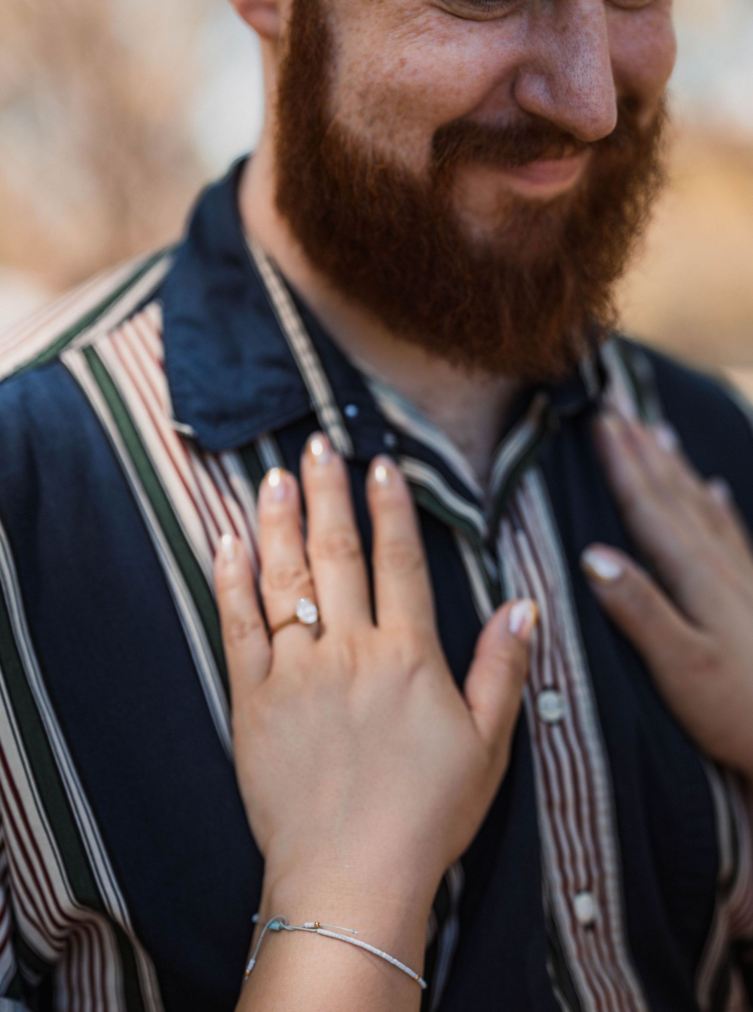 Close-up of womans hand with engagement ring resting on mans striped shirt chest.