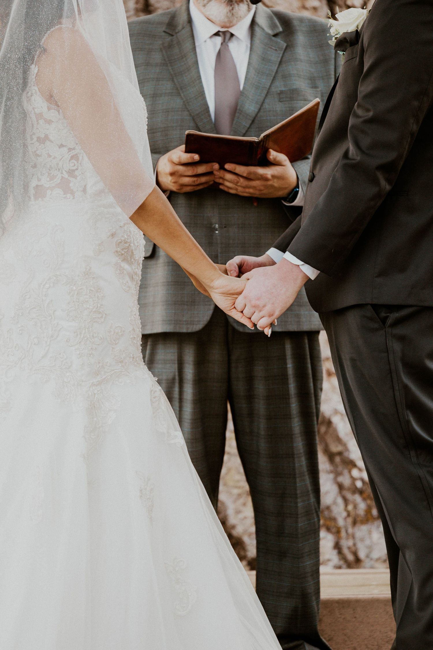 A bride and groom hold hands during their wedding ceremony as an officiant reads from a book.