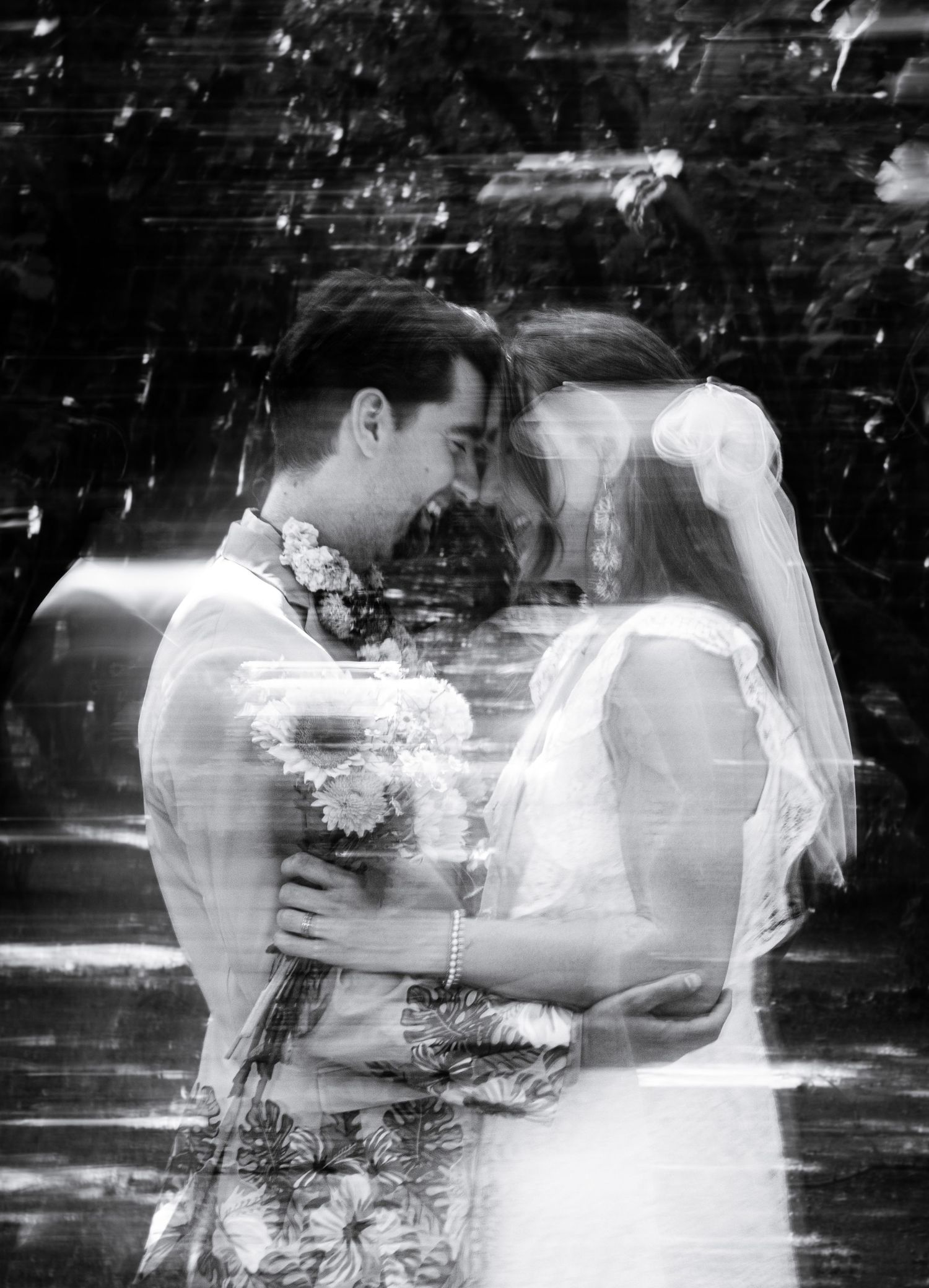 Black and white double exposure wedding photo of bride and groom embracing, holding flowers.