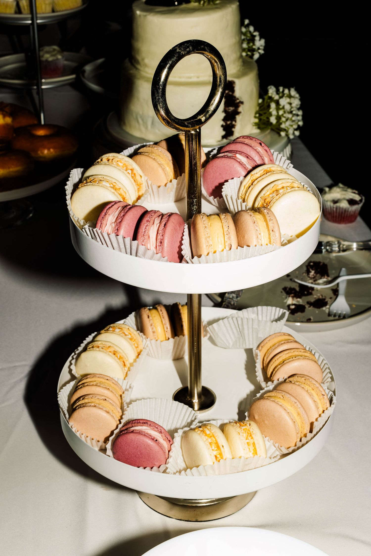 Two-tiered gold and white dessert stand filled with colorful pink and ivory French macarons at wedding.