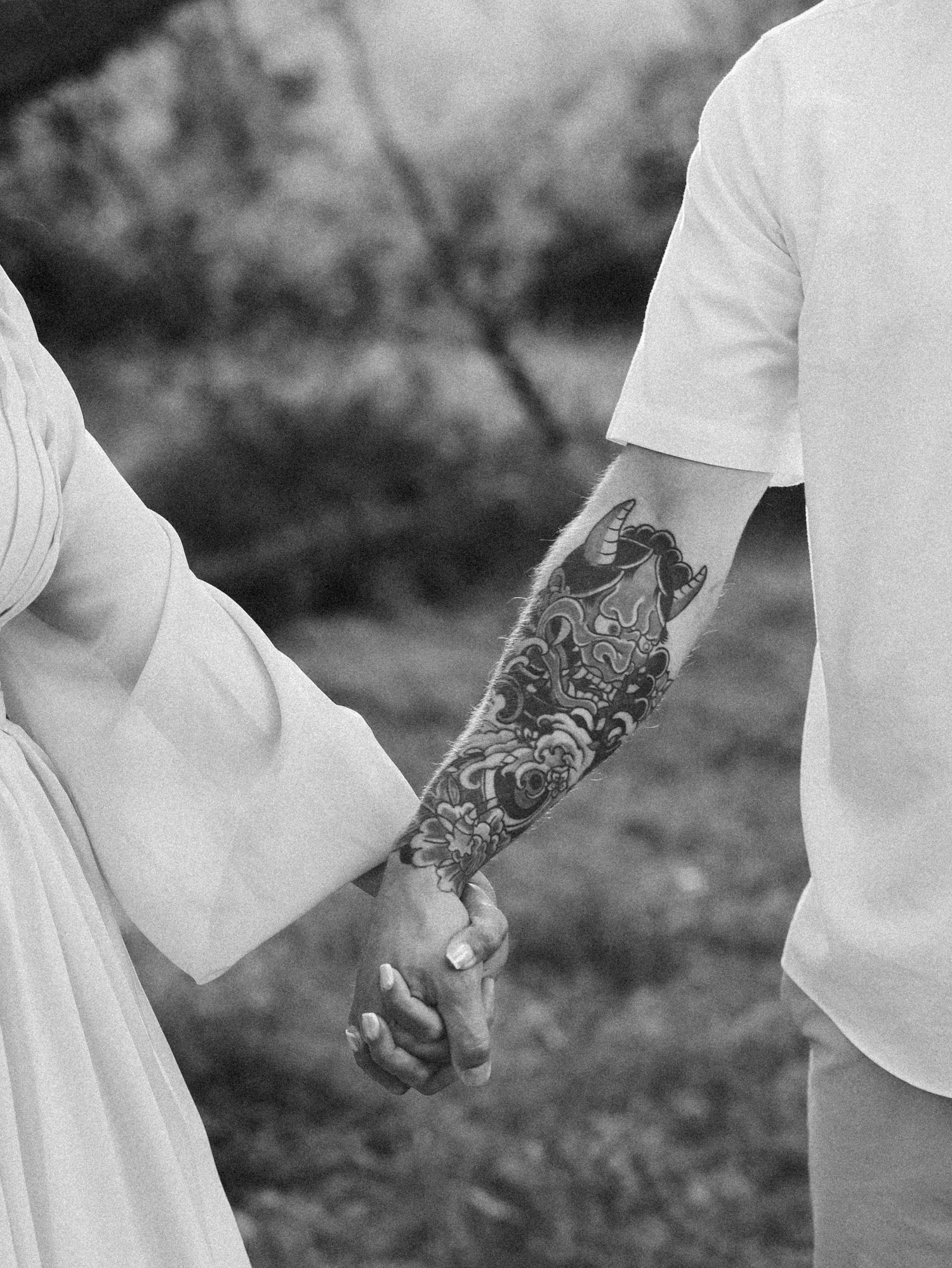 Black and white photo of couple holding hands, man displaying detailed sleeve tattoo artwork.