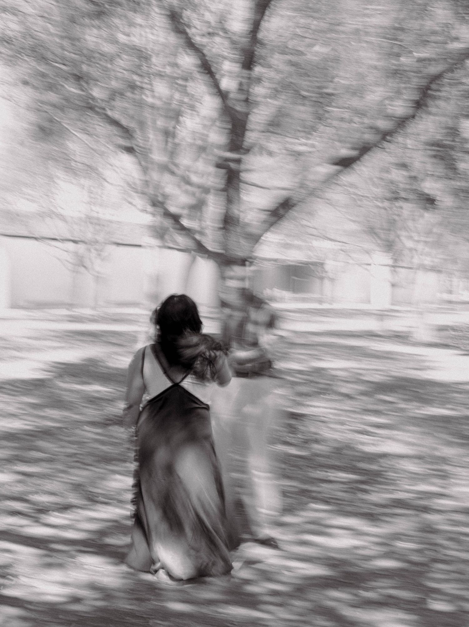 Artistic blurred black and white photo of a woman in a flowing dress under bare trees.