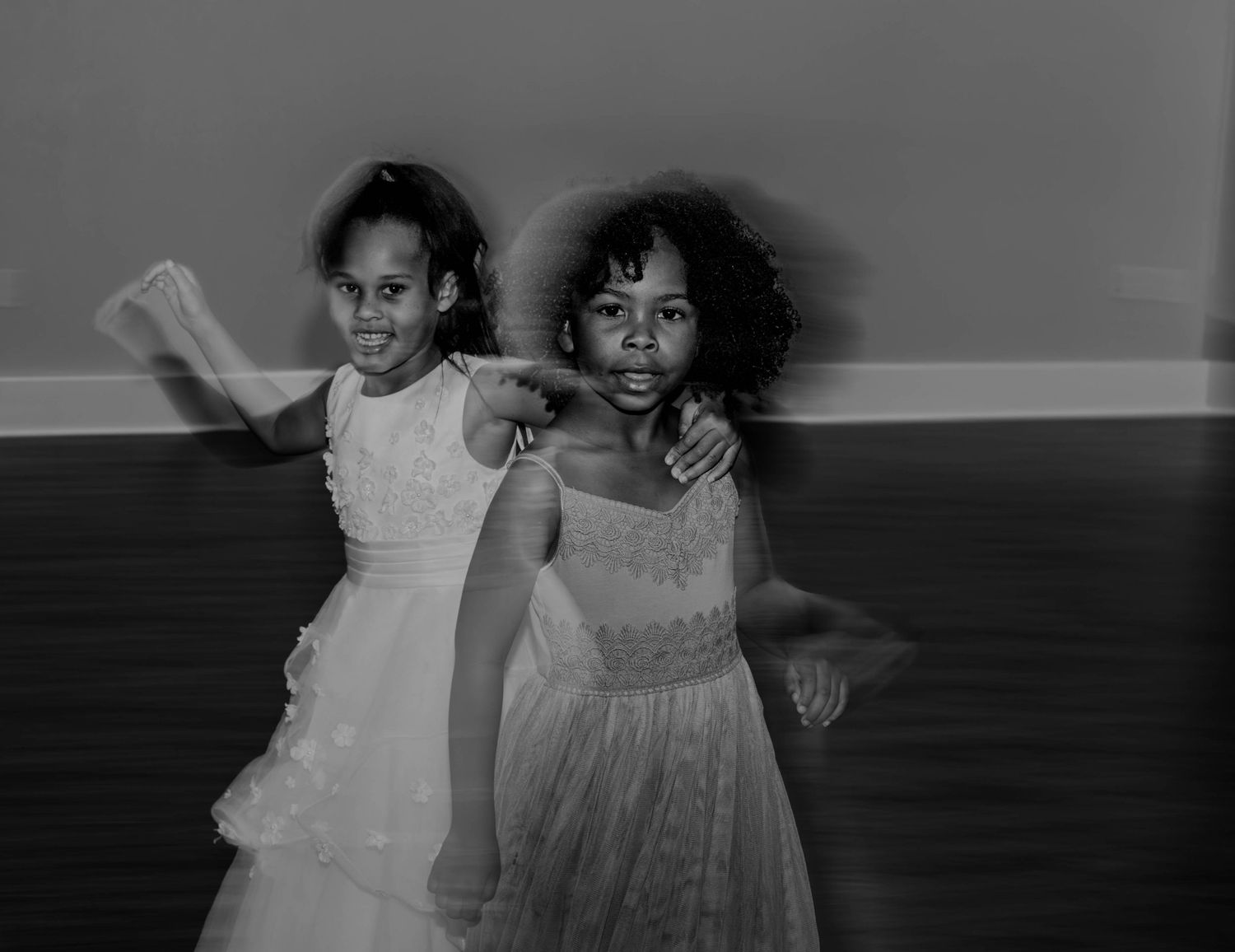 Two young flower girls in white dresses posing together on the dance floor at a wedding reception.