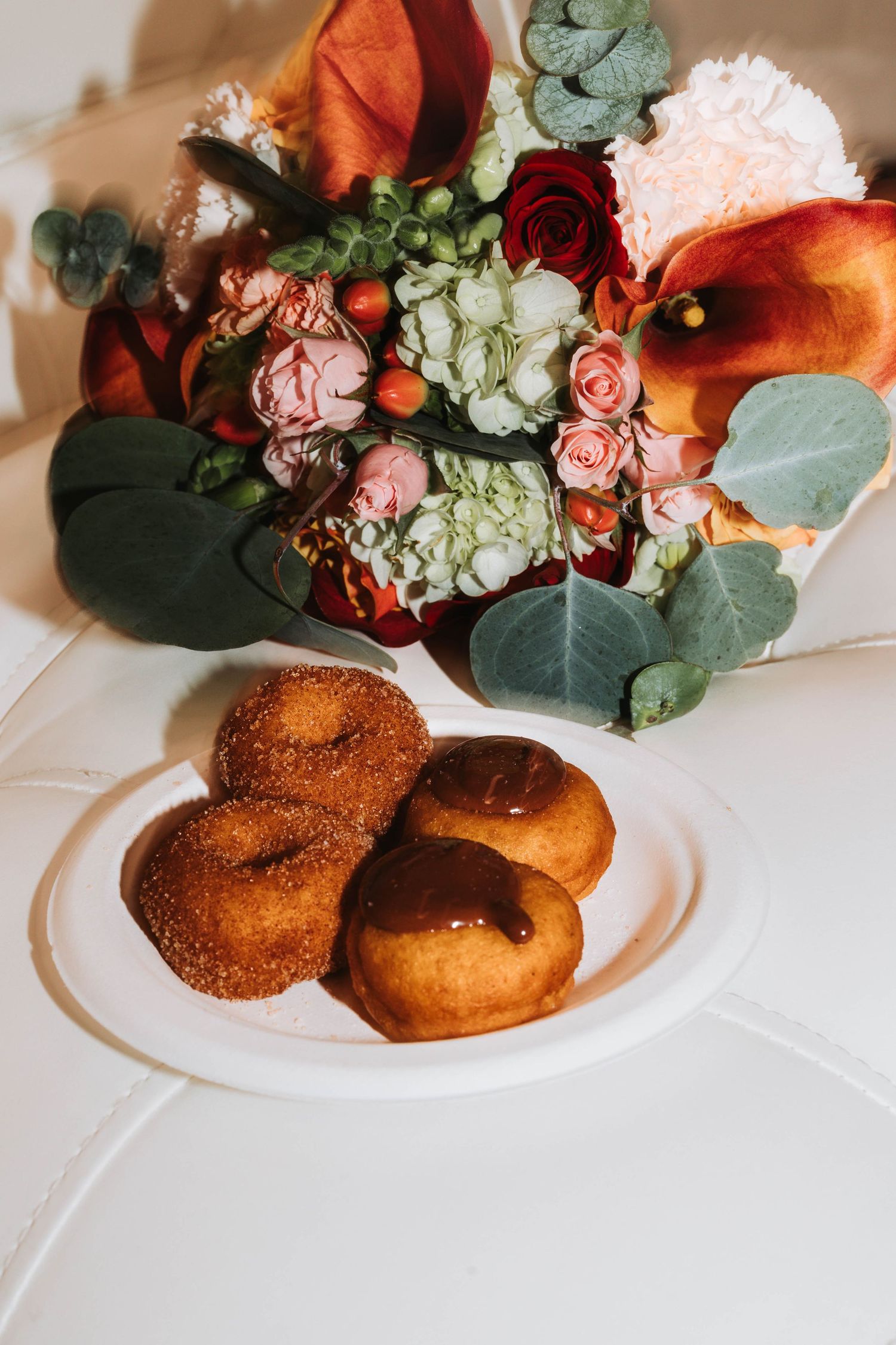 Cinnamon sugar donuts with chocolate sauce on a white plate beside a colorful bridal bouquet.