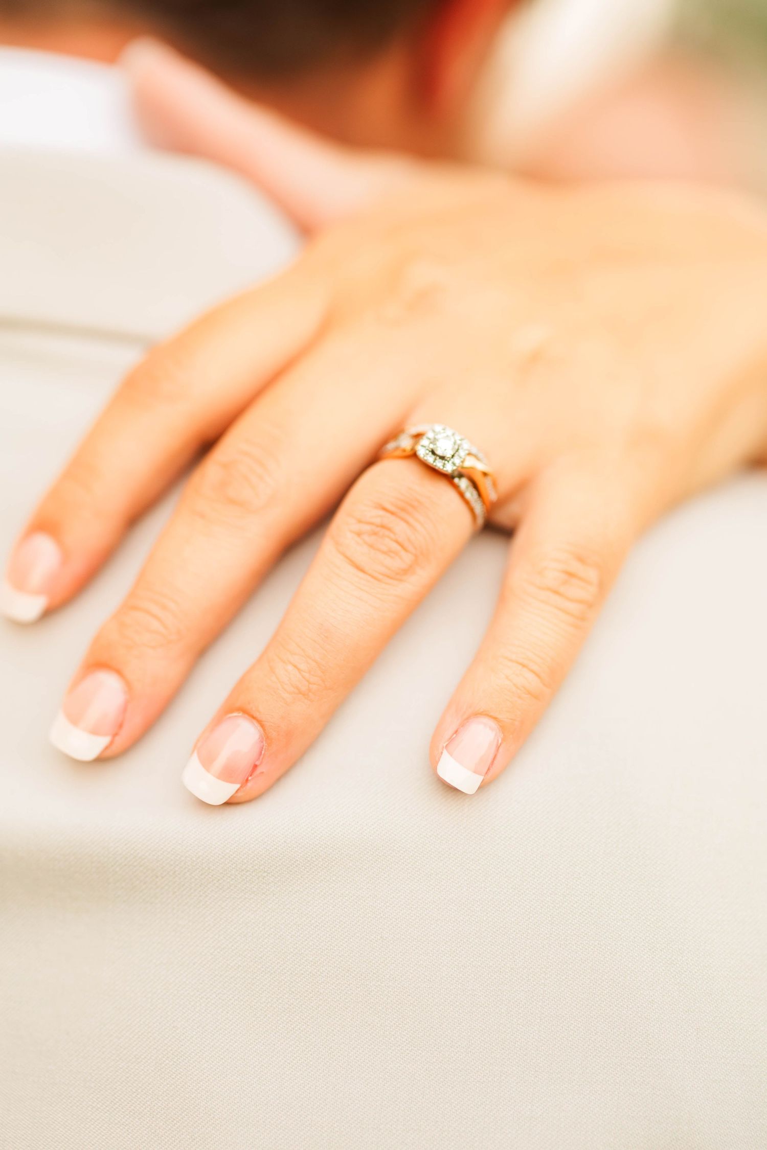 Close-up of bride's hand with elegant diamond engagement ring and French manicure resting on groom.