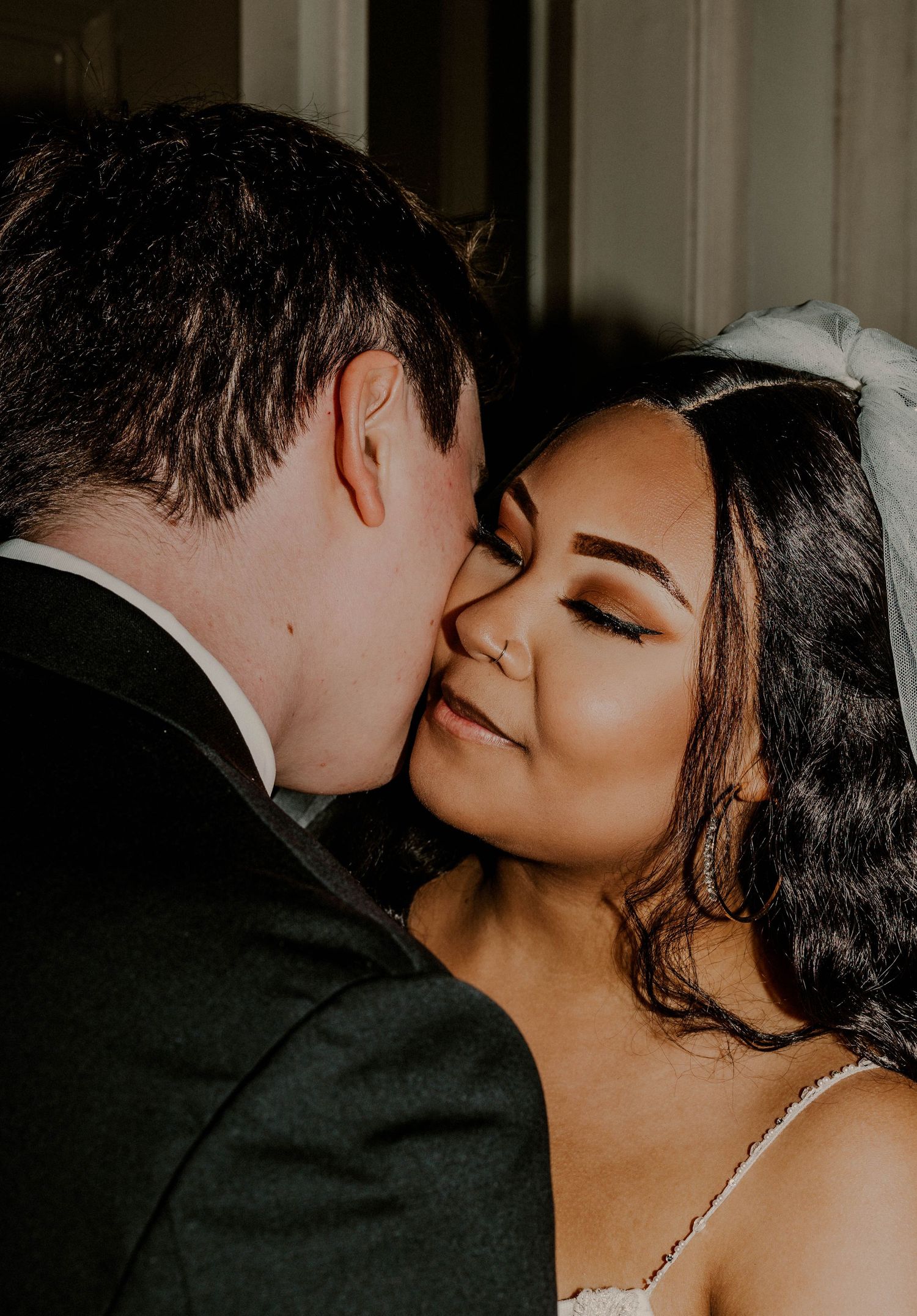 Groom tenderly kissing the cheek of his smiling bride in a close romantic wedding portrait.