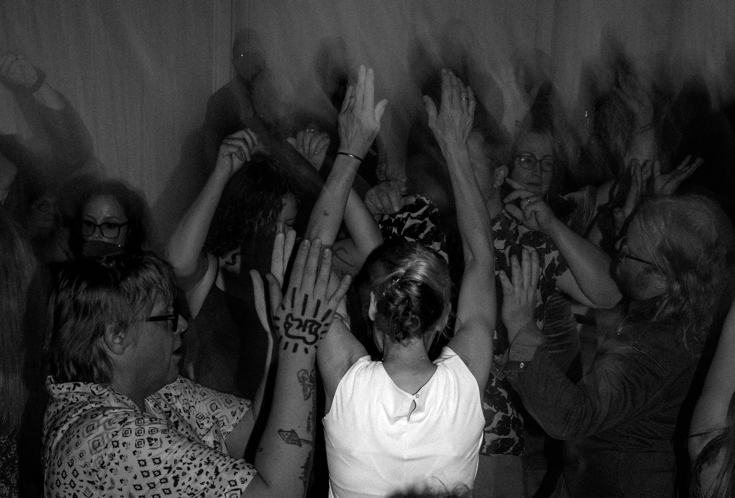 Black and white photo of wedding guests raising their hands and dancing joyfully together.