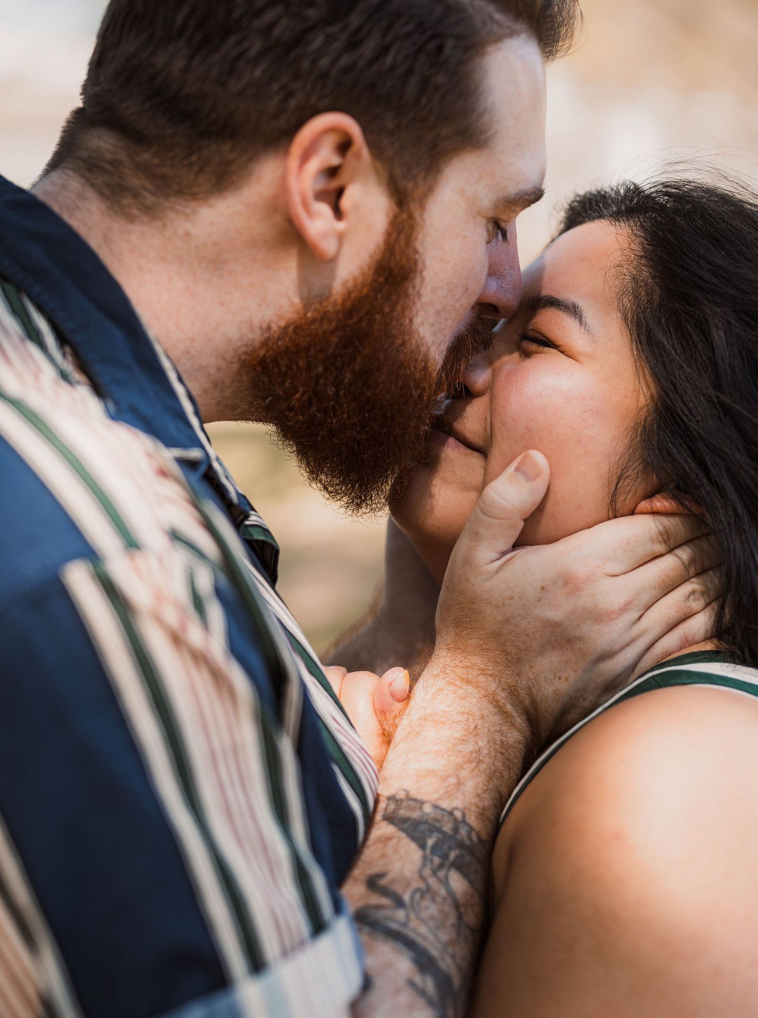 Close-up of bearded man gently holding womans face while sharing a romantic kiss.