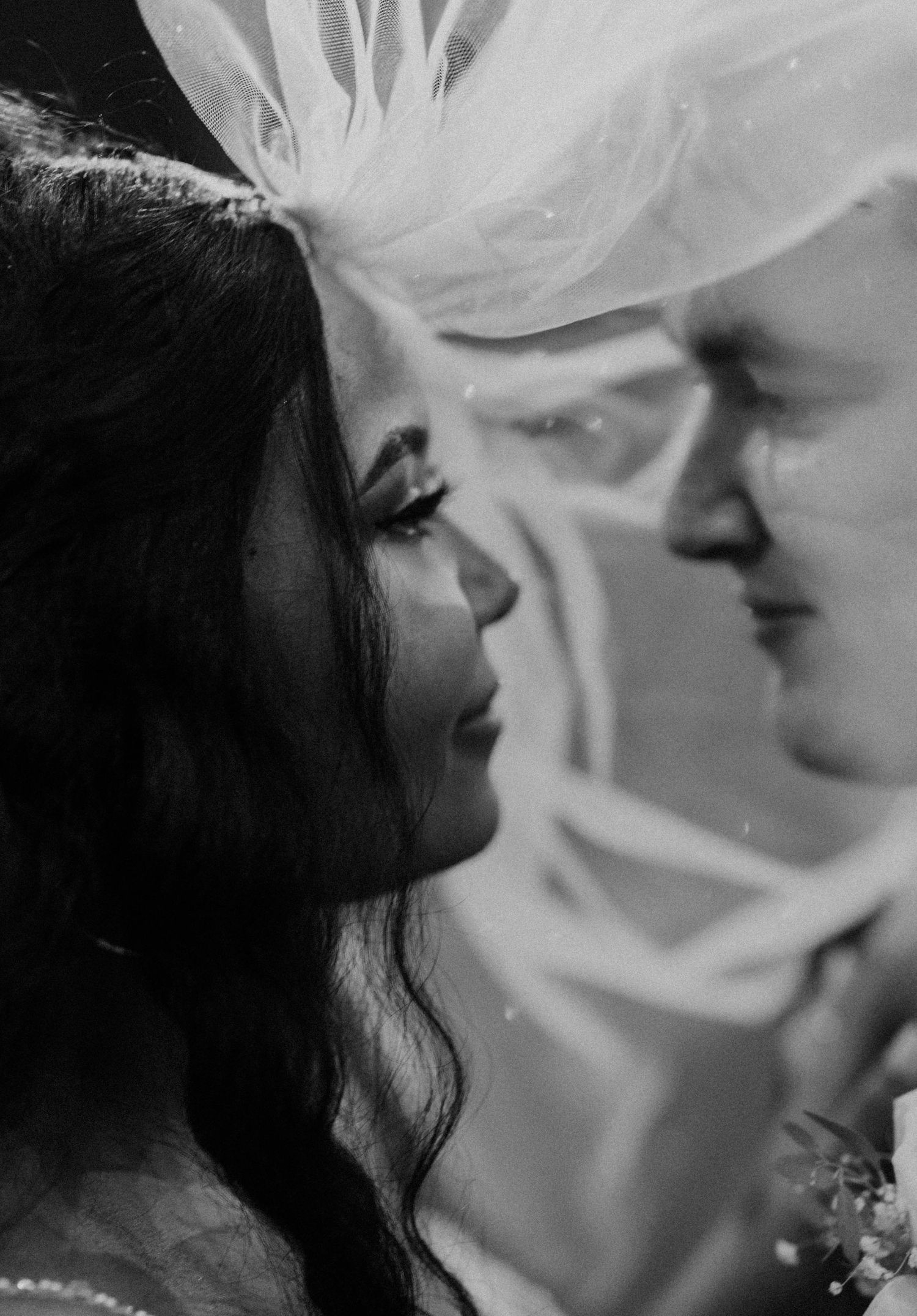 Intimate black and white close-up of bride and groom nearly kissing beneath the bride's veil.