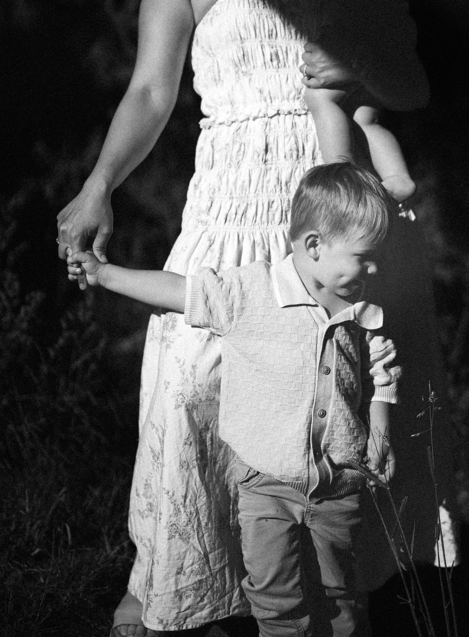 Black and white photo of young boy holding mothers hand outdoors in natural setting.