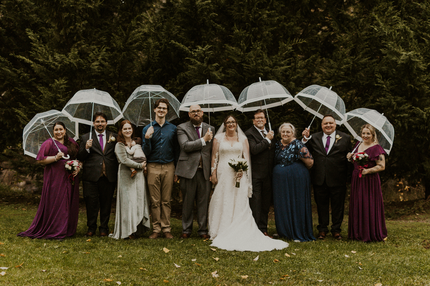 Wedding party holding clear bubble umbrellas in purple and navy attire outdoors.