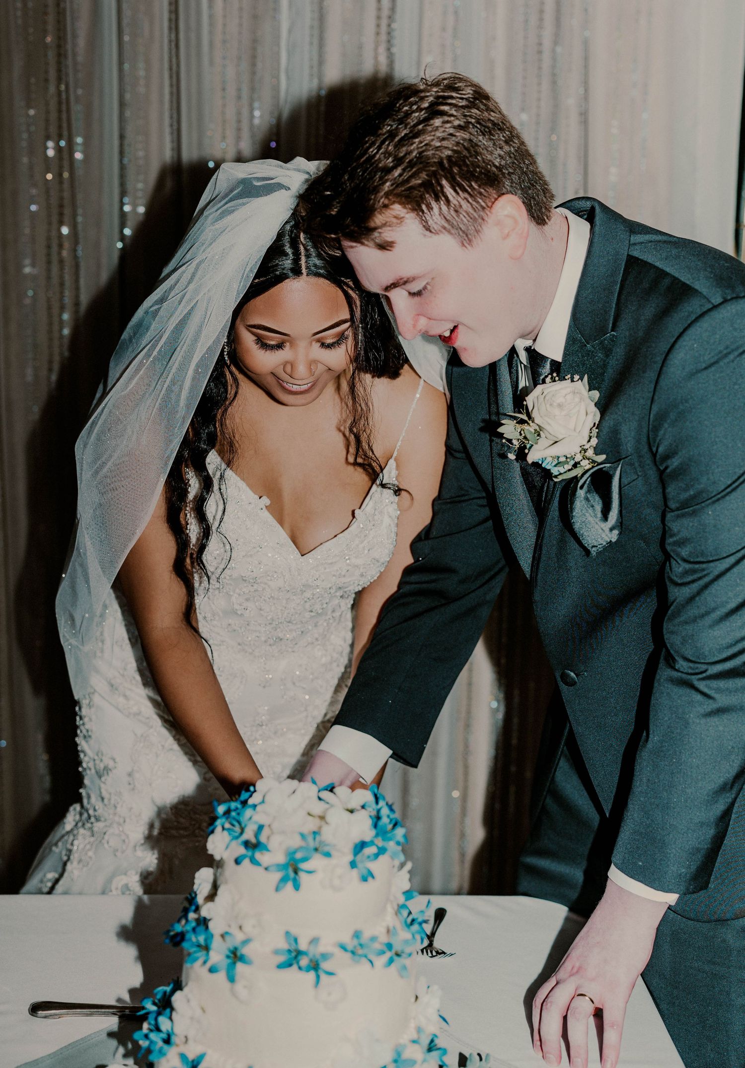 Bride and groom cutting their white wedding cake decorated with blue flowers at their reception.