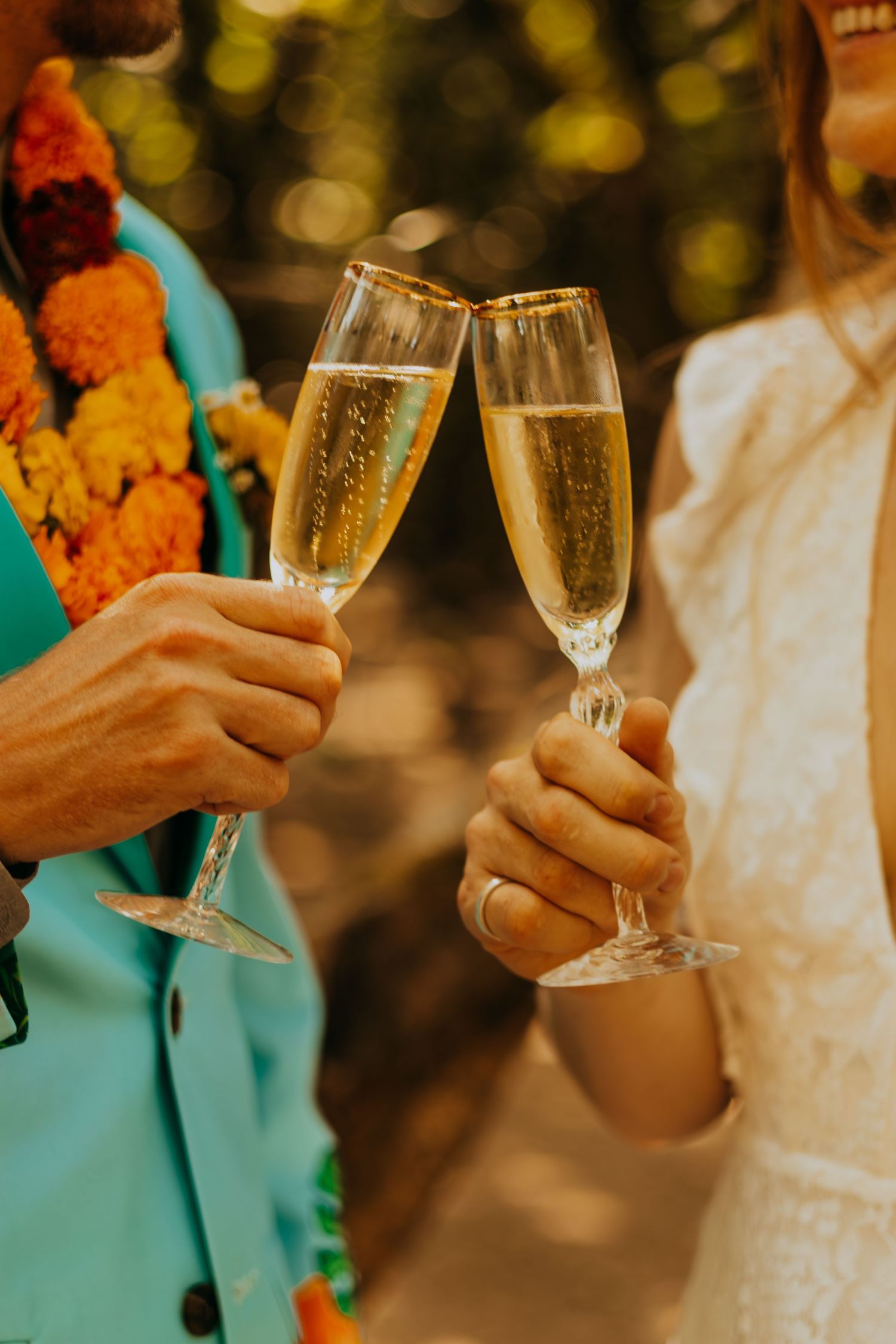 Bride and groom clink champagne flutes in a celebratory toast at their colorful outdoor wedding ceremony.