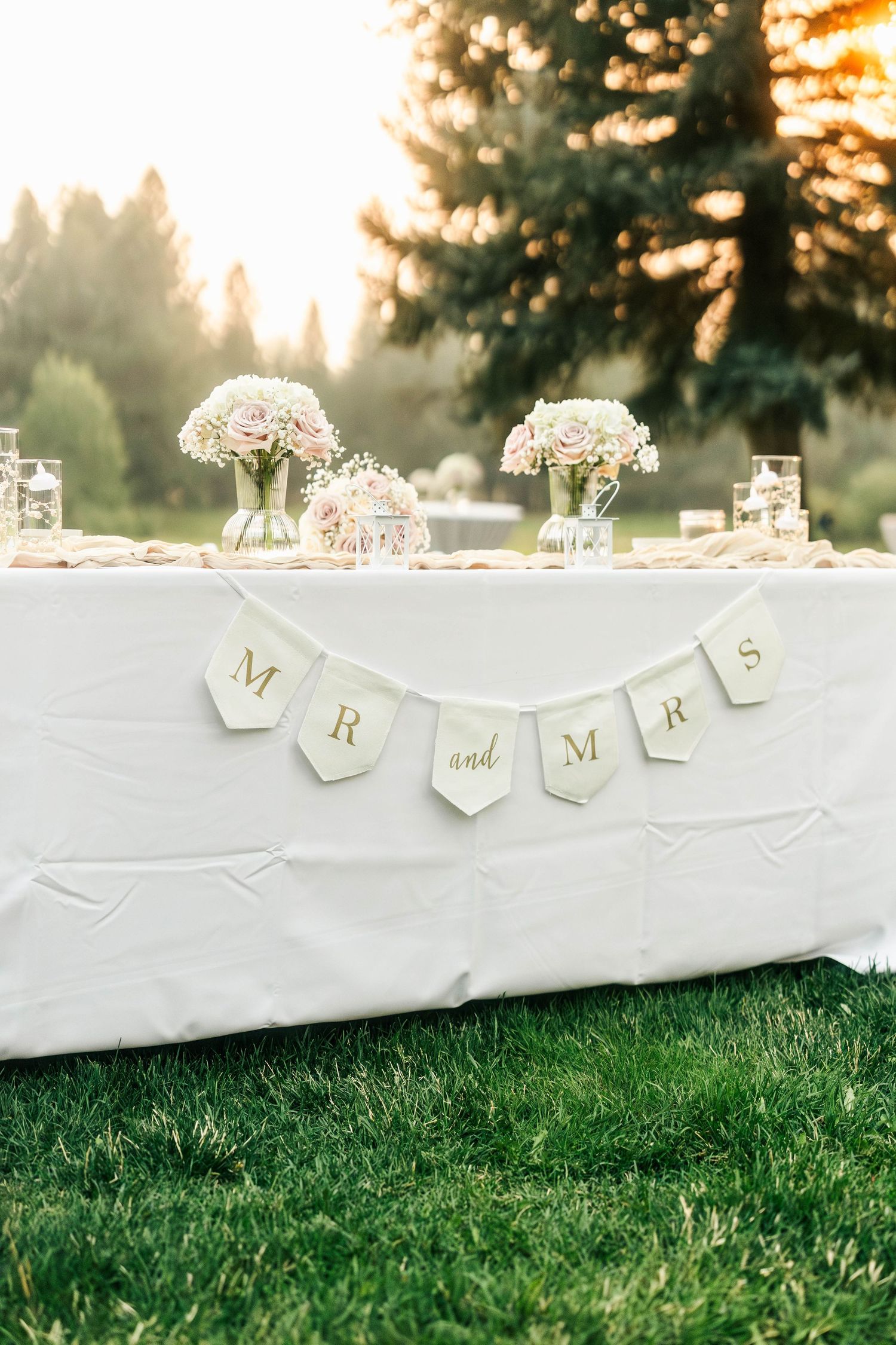 Outdoor wedding sweetheart table decorated with Mr and Mrs banner and blush pink floral arrangements.