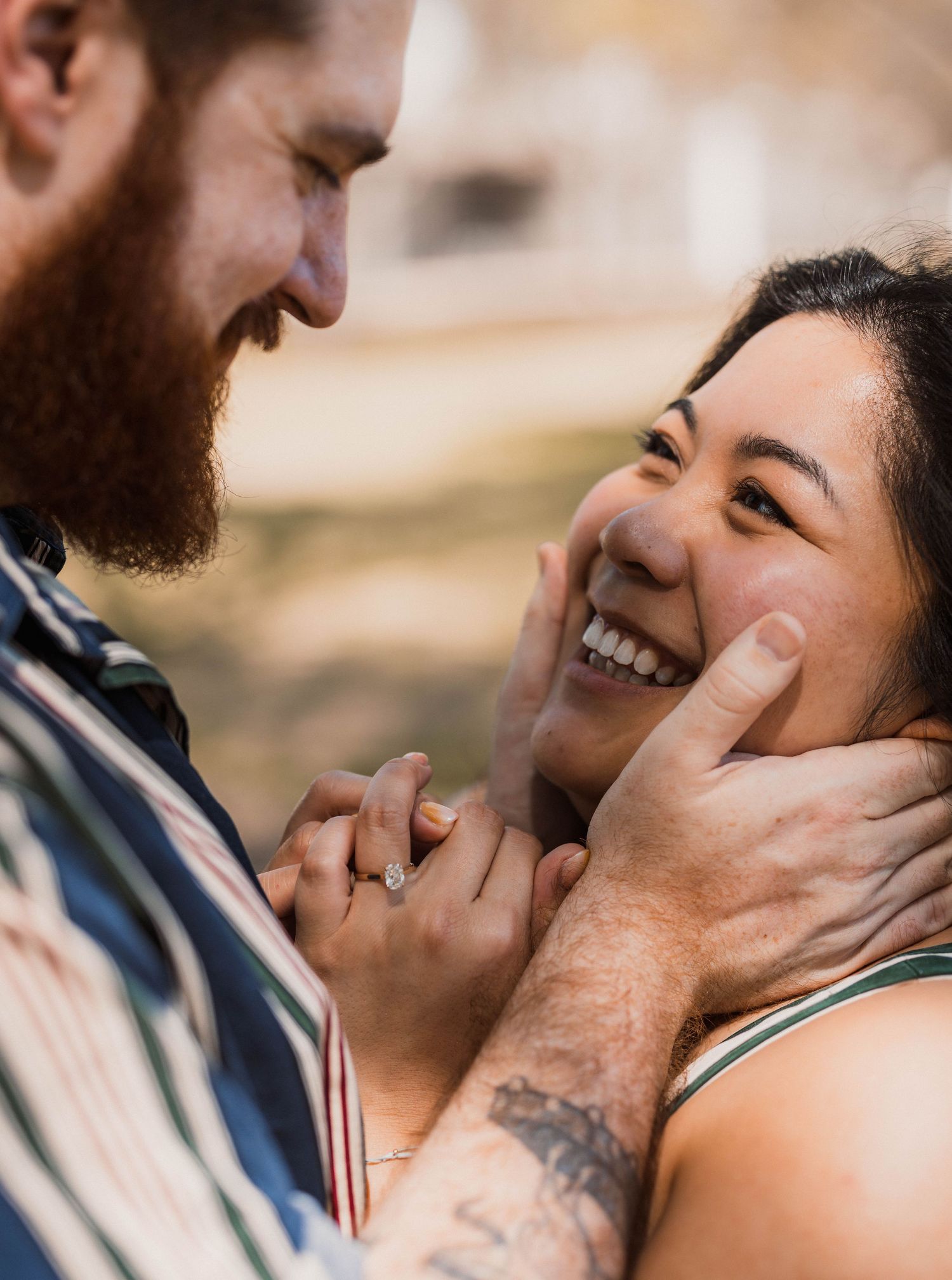 Joyful woman laughing as bearded man tenderly cups her face while holding hands.