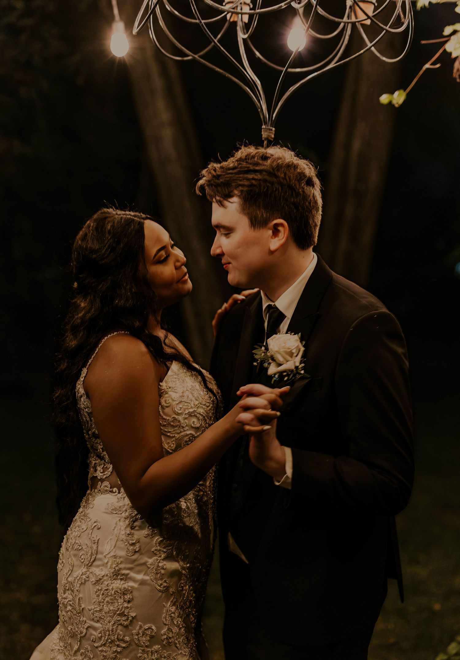 Bride and groom share an intimate moment dancing under a chandelier at their romantic outdoor evening wedding.
