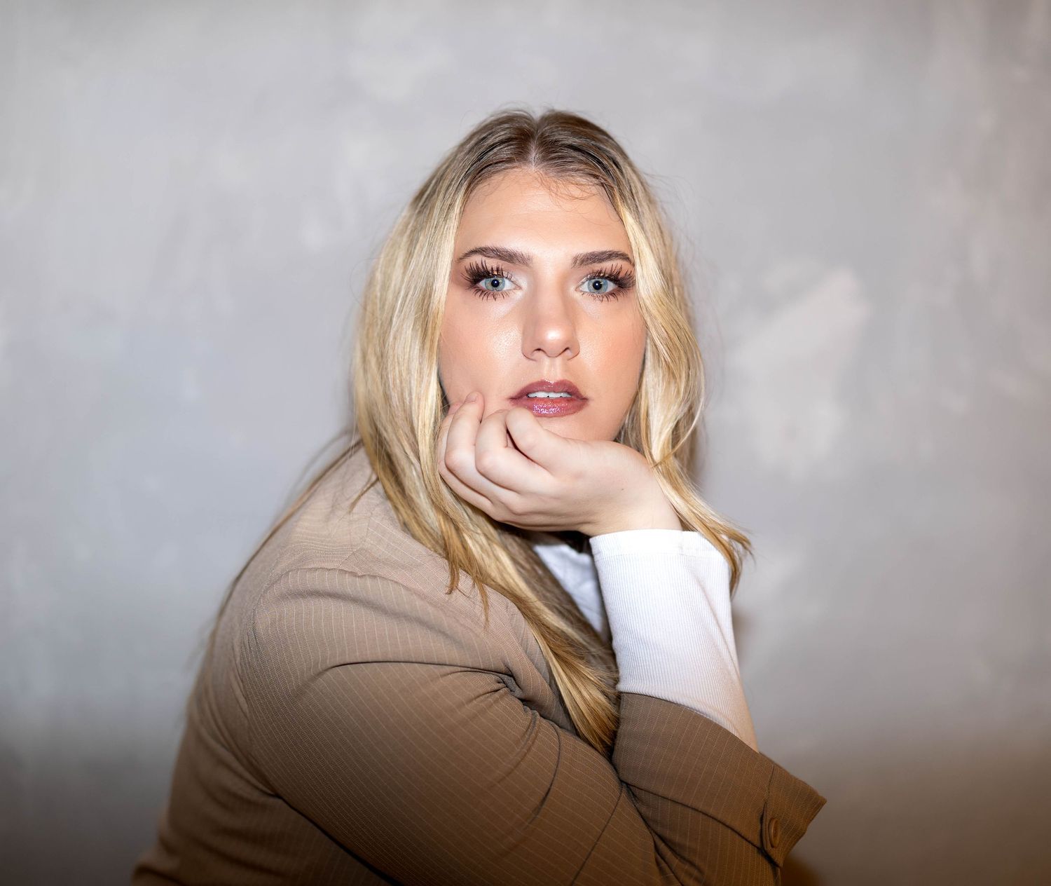 Black and white portrait of confident blonde woman in blazer resting chin on hand.
