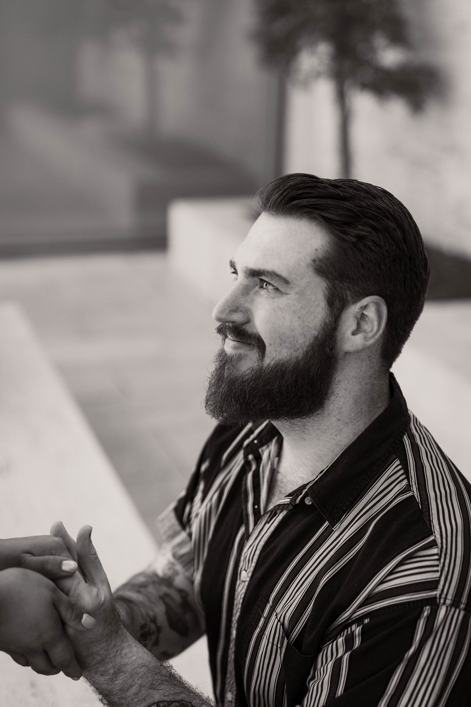 Black and white portrait of a bearded man in a striped shirt smiling and looking away.