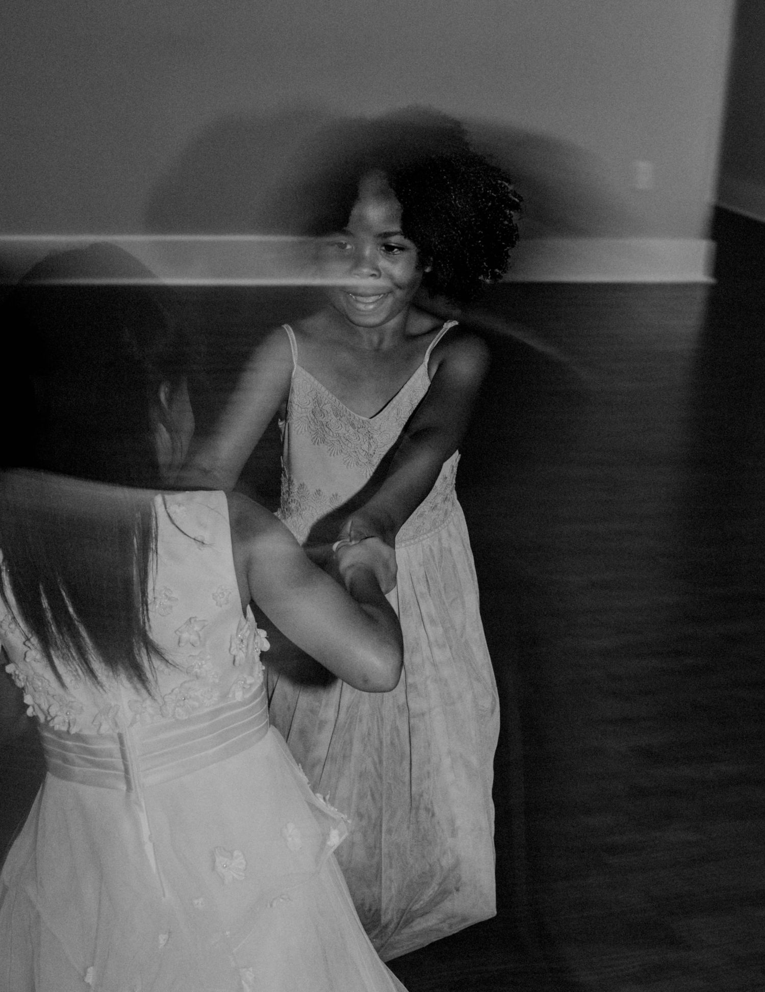 Black and white photo of two young flower girls dancing joyfully at a wedding reception.