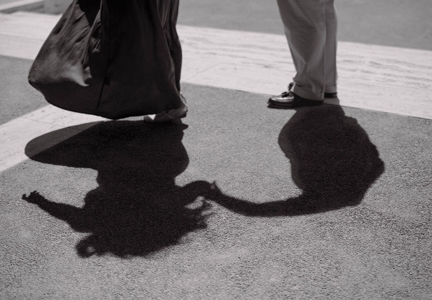 Black and white photo of two people casting shadows on pavement at crosswalk.