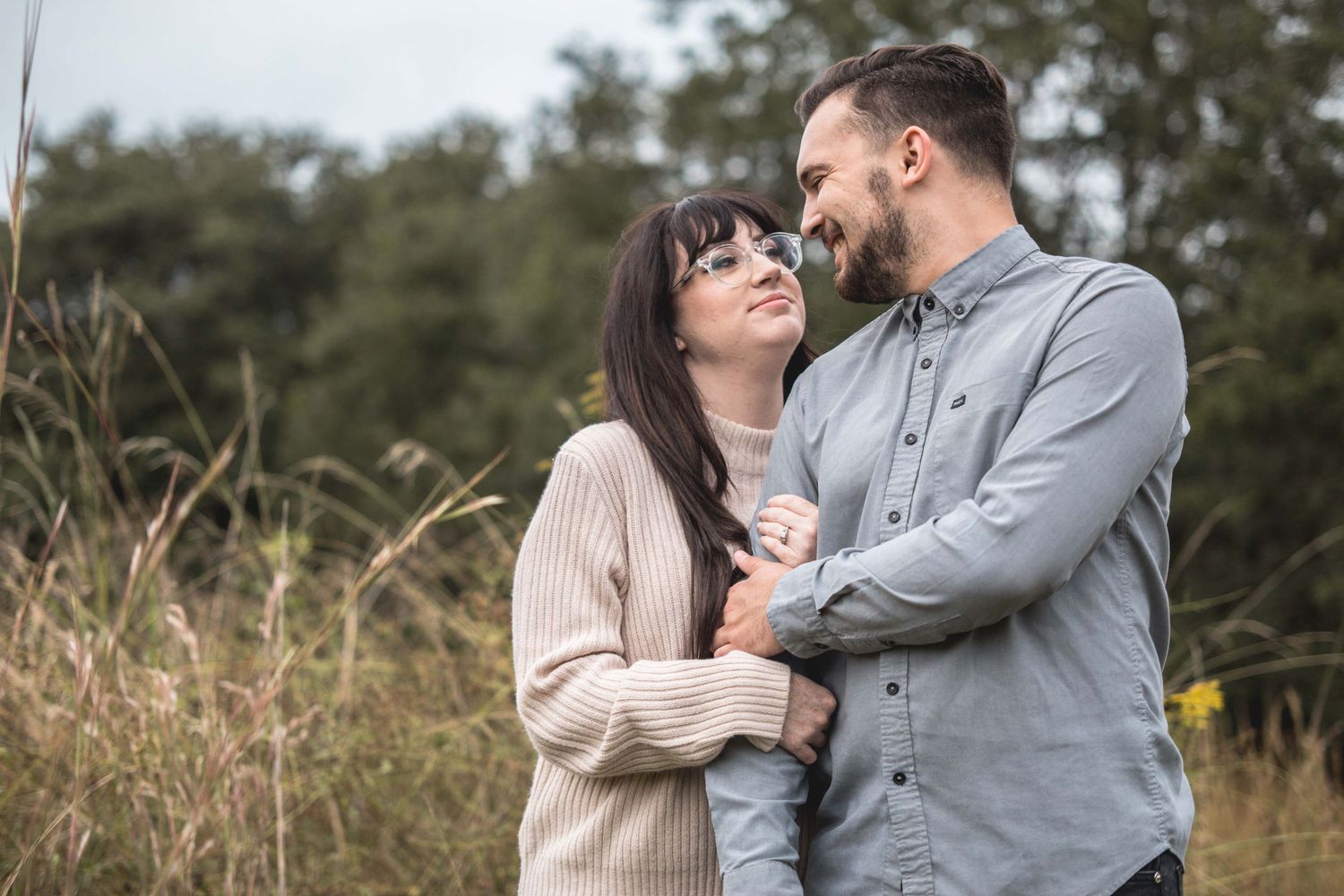 Happy couple embraces and gazes at each other in a natural outdoor field setting.