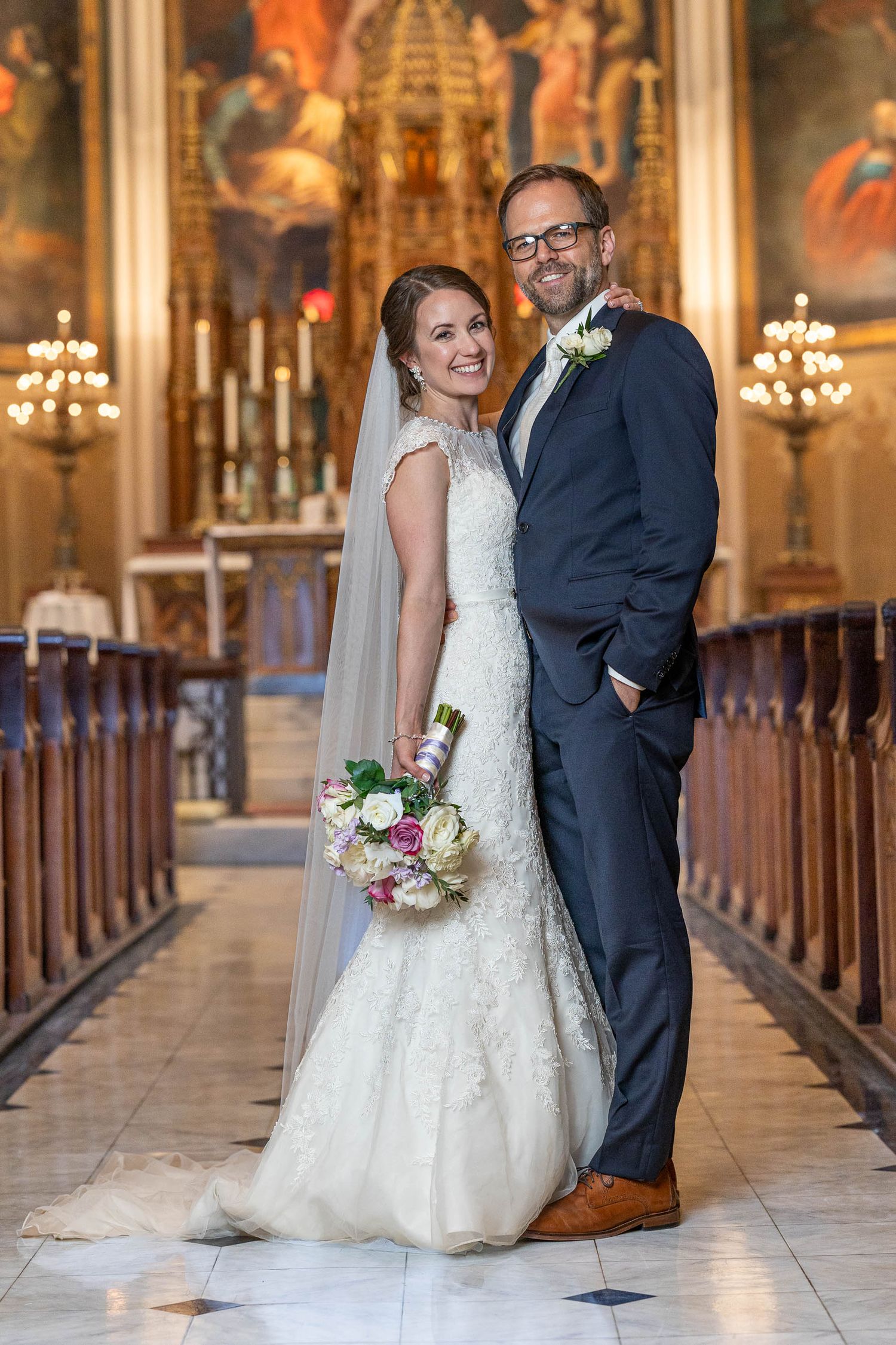 Smiling bride and groom posing together inside a grand ornate church with golden altar backdrop.