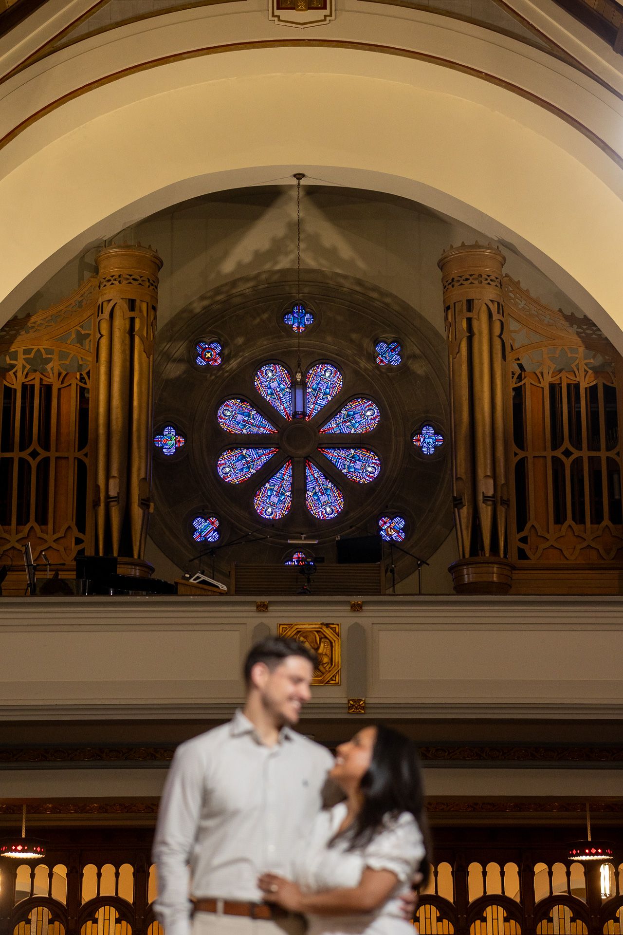 Couple embraces in a church with a stunning blue rose window stained glass above them.