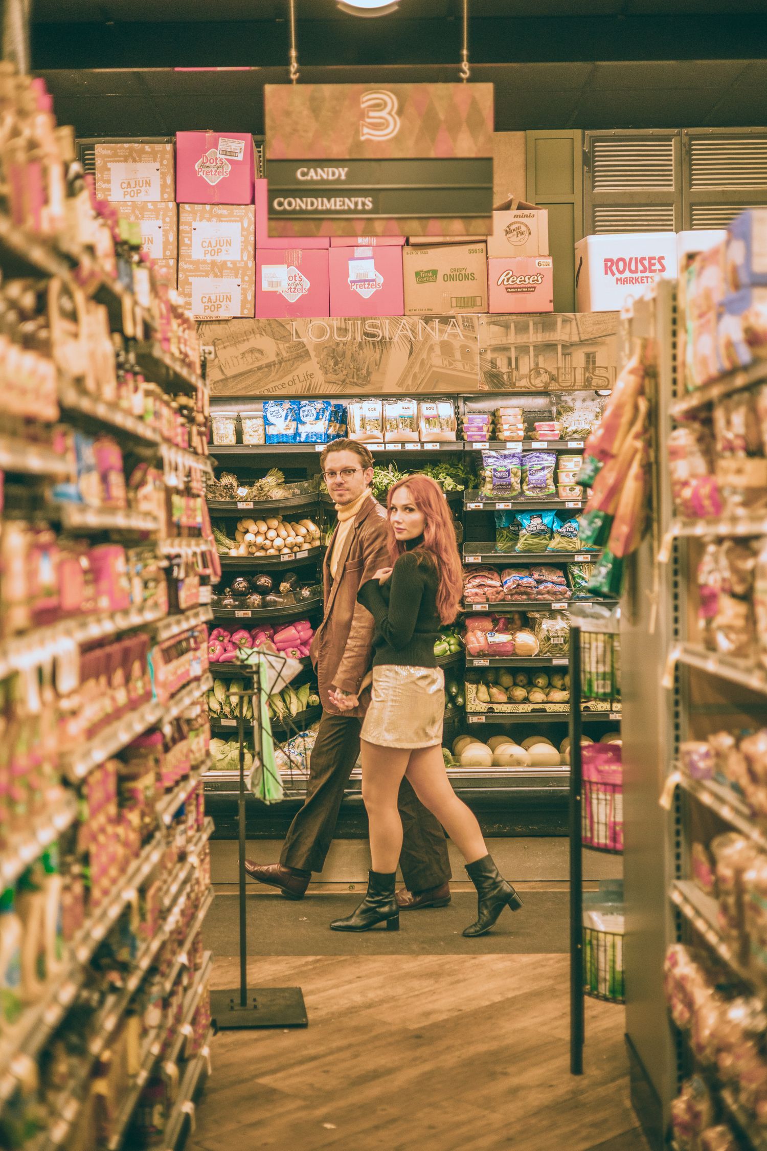 Couple posing together in grocery store candy aisle at Rouses Market, woman with red hair wearing mini skirt and boots.