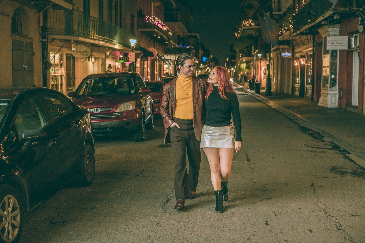 Couple walking together on a vibrant city street at night, illuminated by warm lights and neon signs.