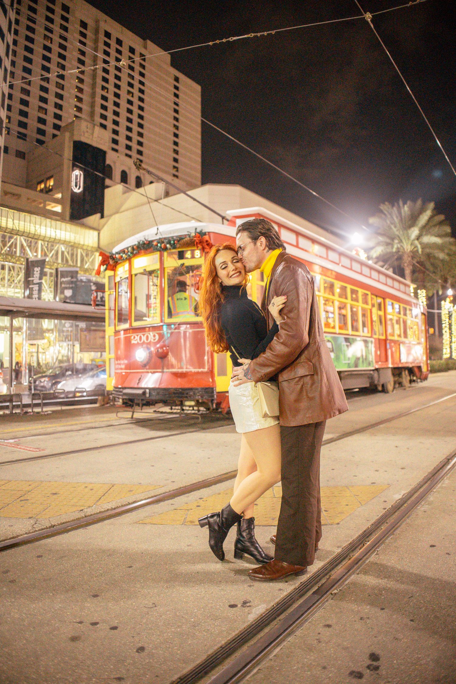 Couple embracing romantically at night in front of a red streetcar on city tracks, New Orleans.