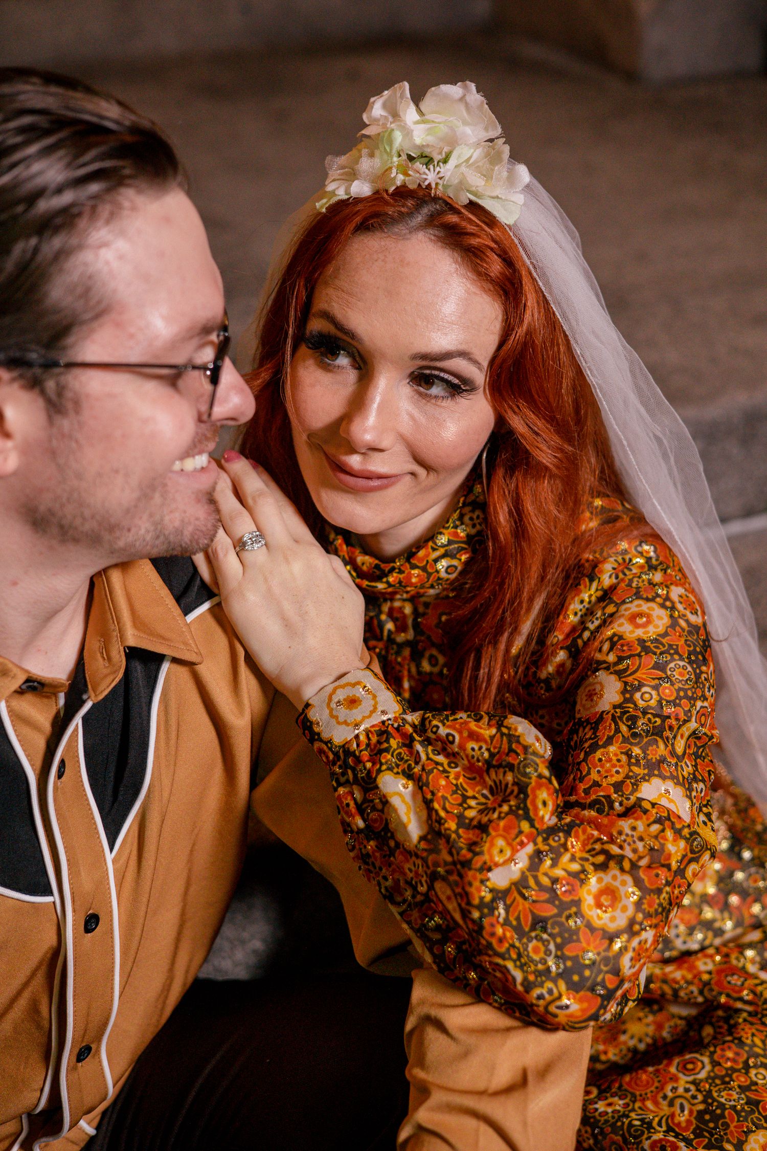 Bride in floral dress and veil with groom in mustard shirt sharing a romantic moment.
