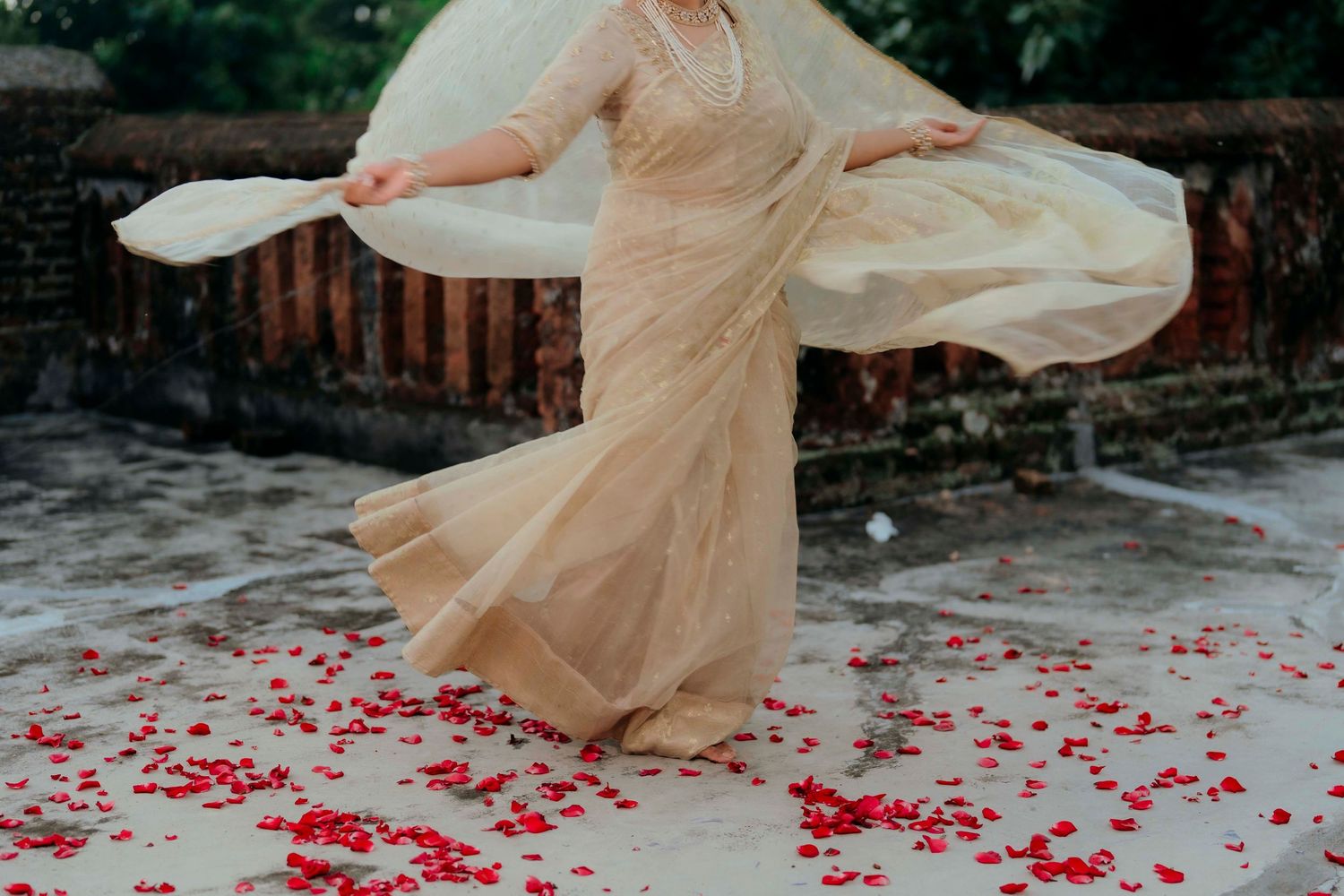 Bride twirling in golden saree surrounded by red rose petals on ground at Indian wedding.