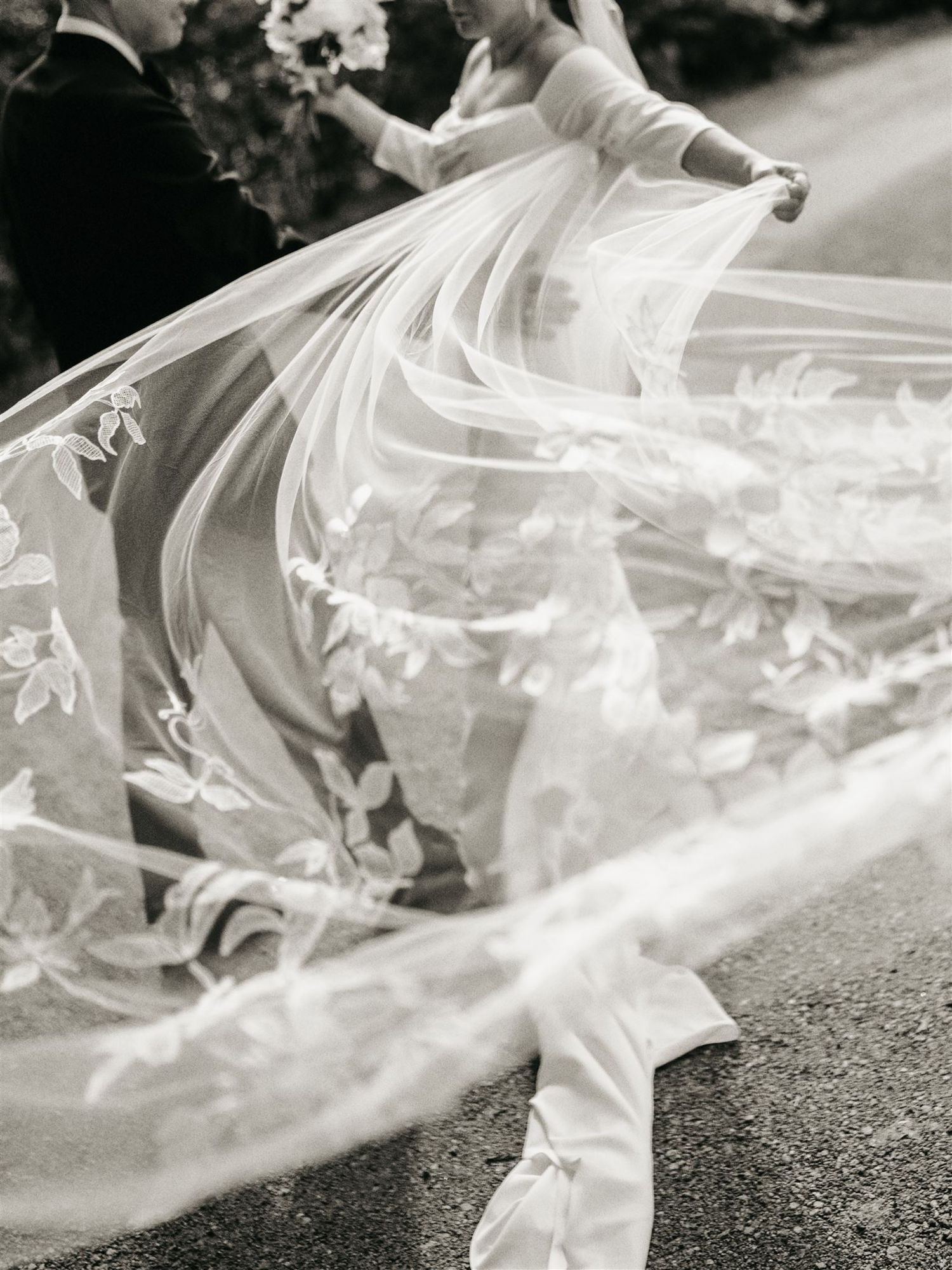 Black and white close-up of a flowing lace embroidered bridal veil billowing dramatically in the wind.